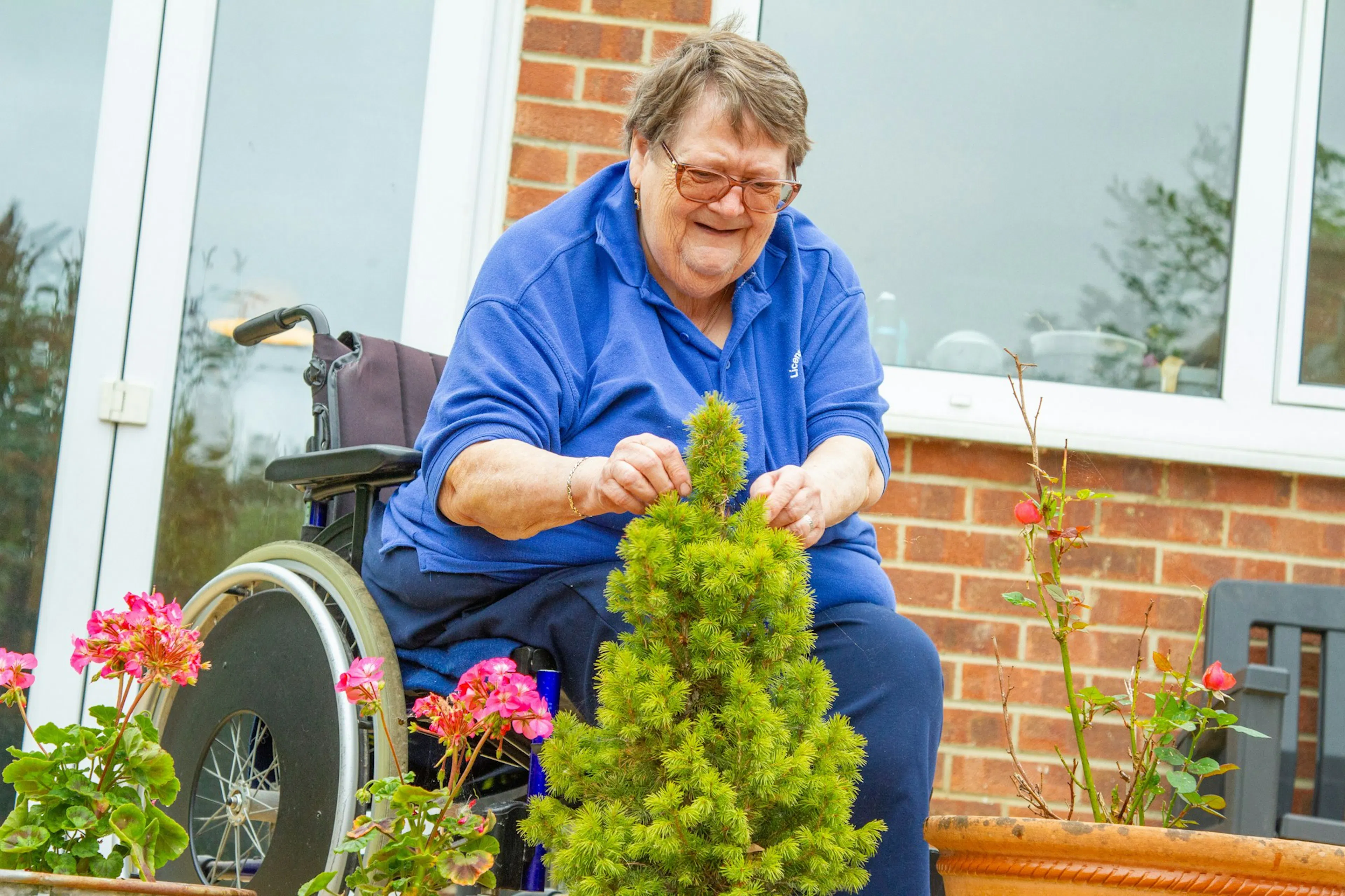 Older woman in a wheelchair tending a potted plant at a raised garden bed during garden therapy