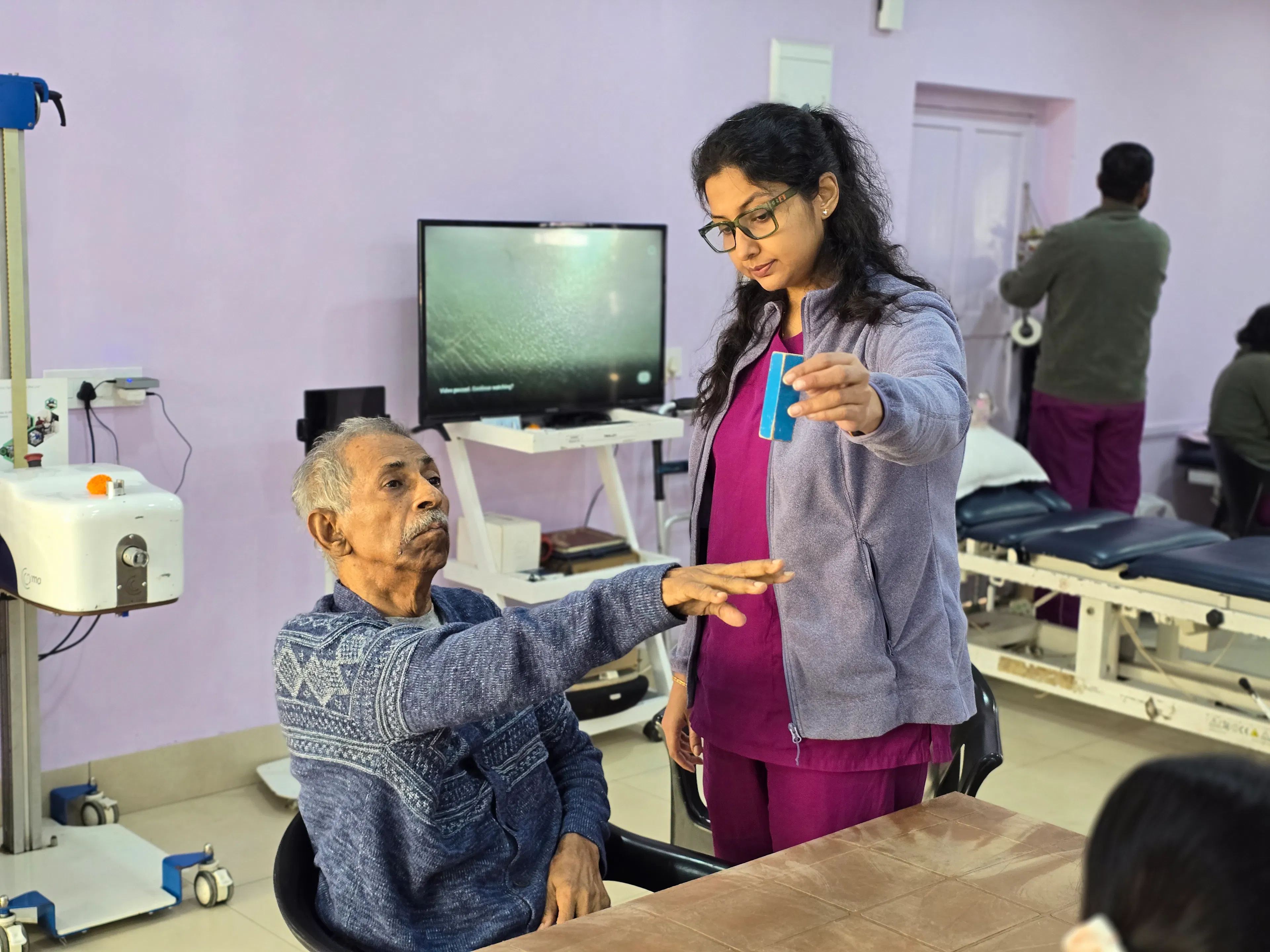 Therapist guiding an older man to raise his arm during screen-based arm practice in virtual reality rehabilitation
