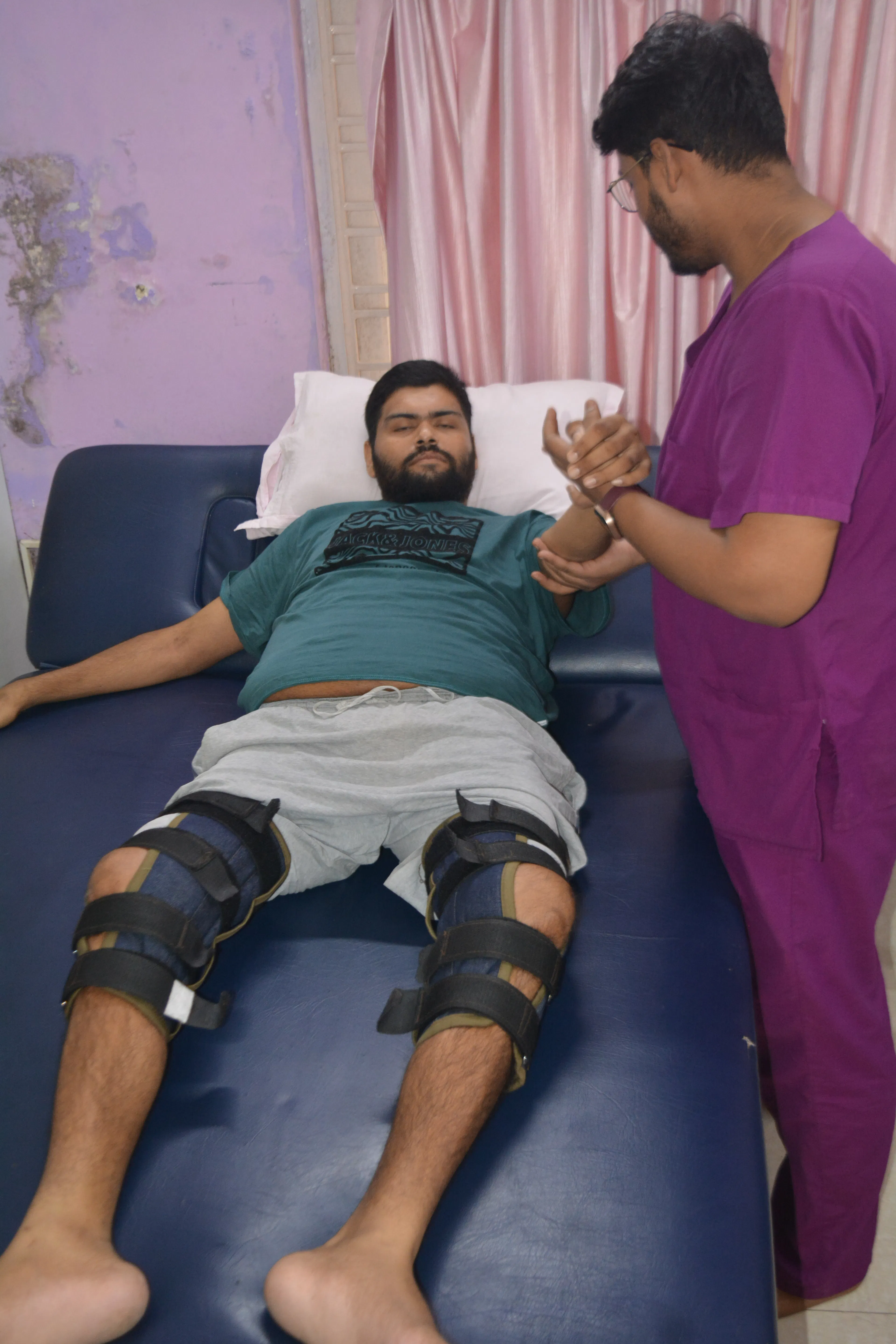 Patient lying with knee splints while a therapist holds his hand during long-term spasticity management