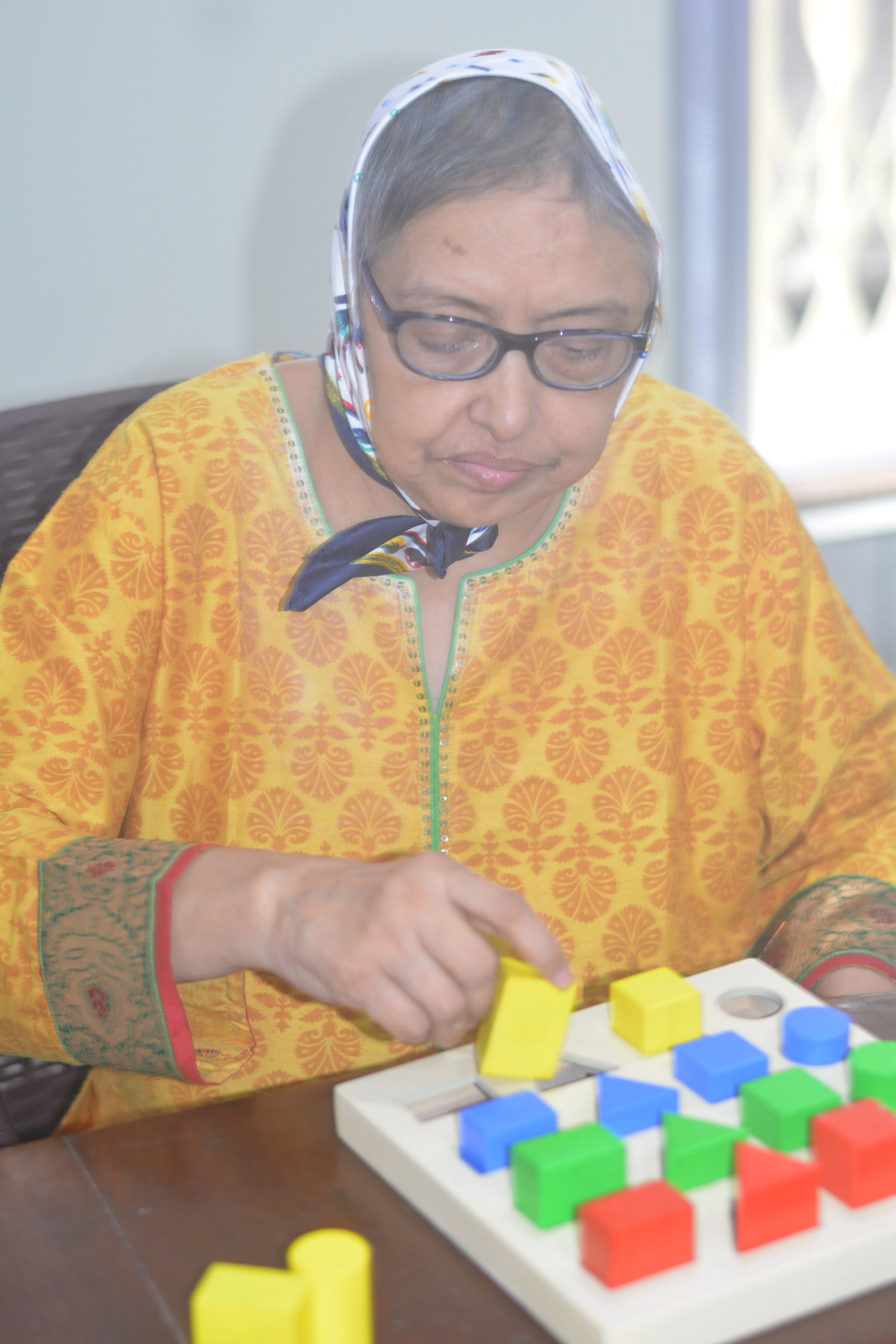 Elderly woman placing coloured shapes on a shape board as she rebuilds hand skills in occupational therapy