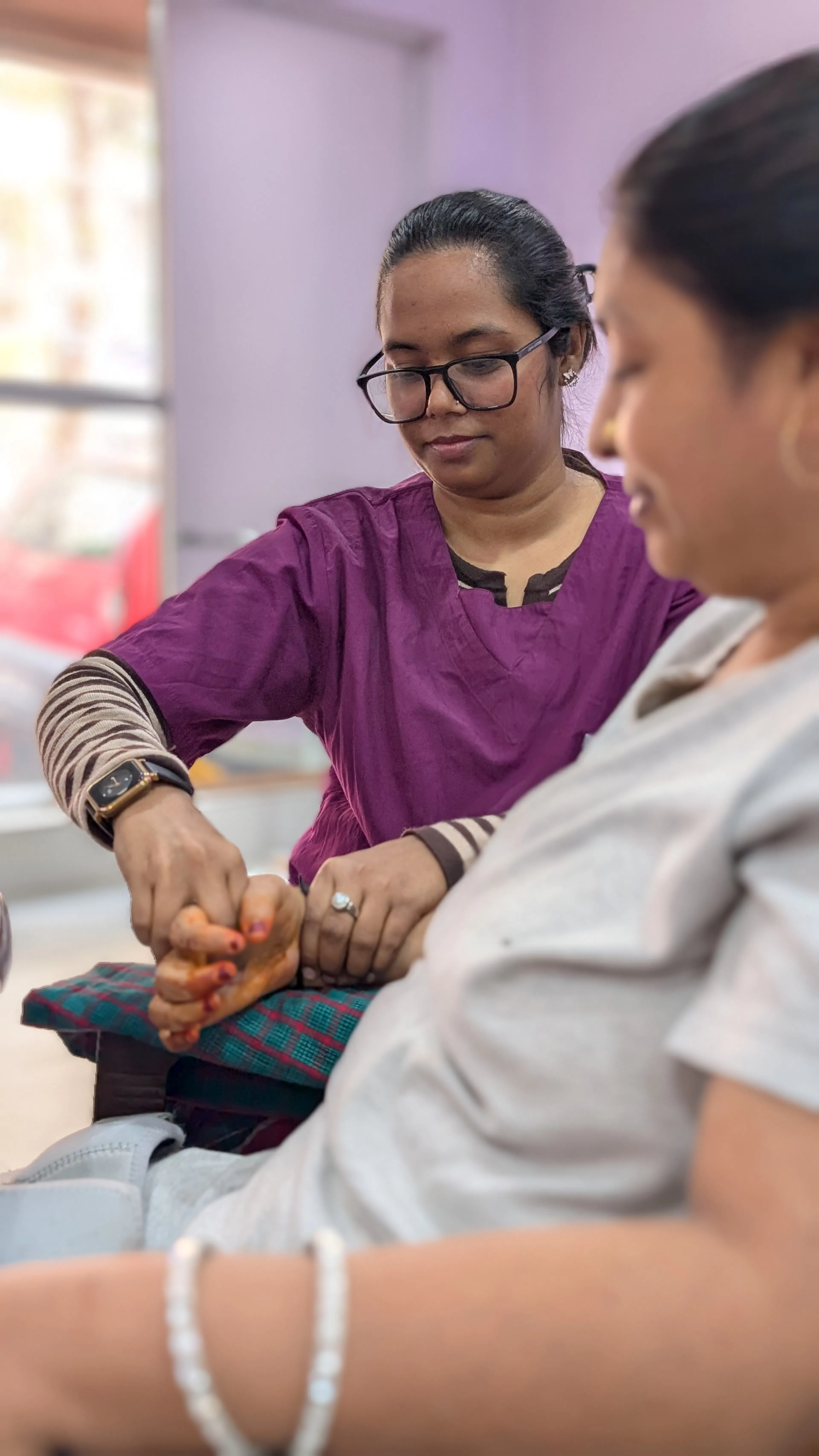 Therapist gently opening a woman's stiff hand and wrist, a common sign of spasticity