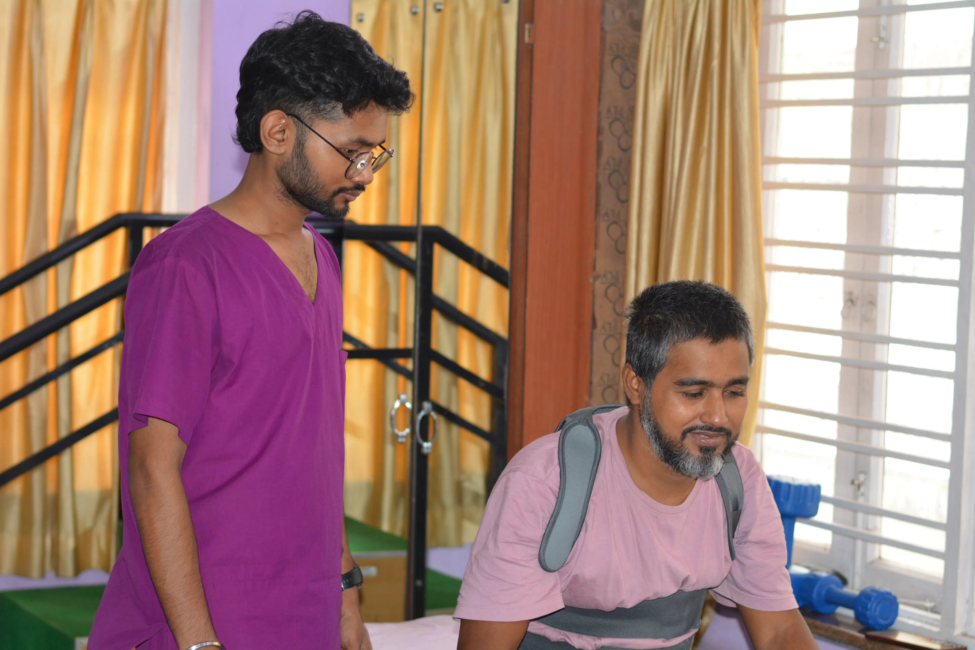 Therapist with a seated man near the parallel bars during a weeks-long inpatient rehab programme