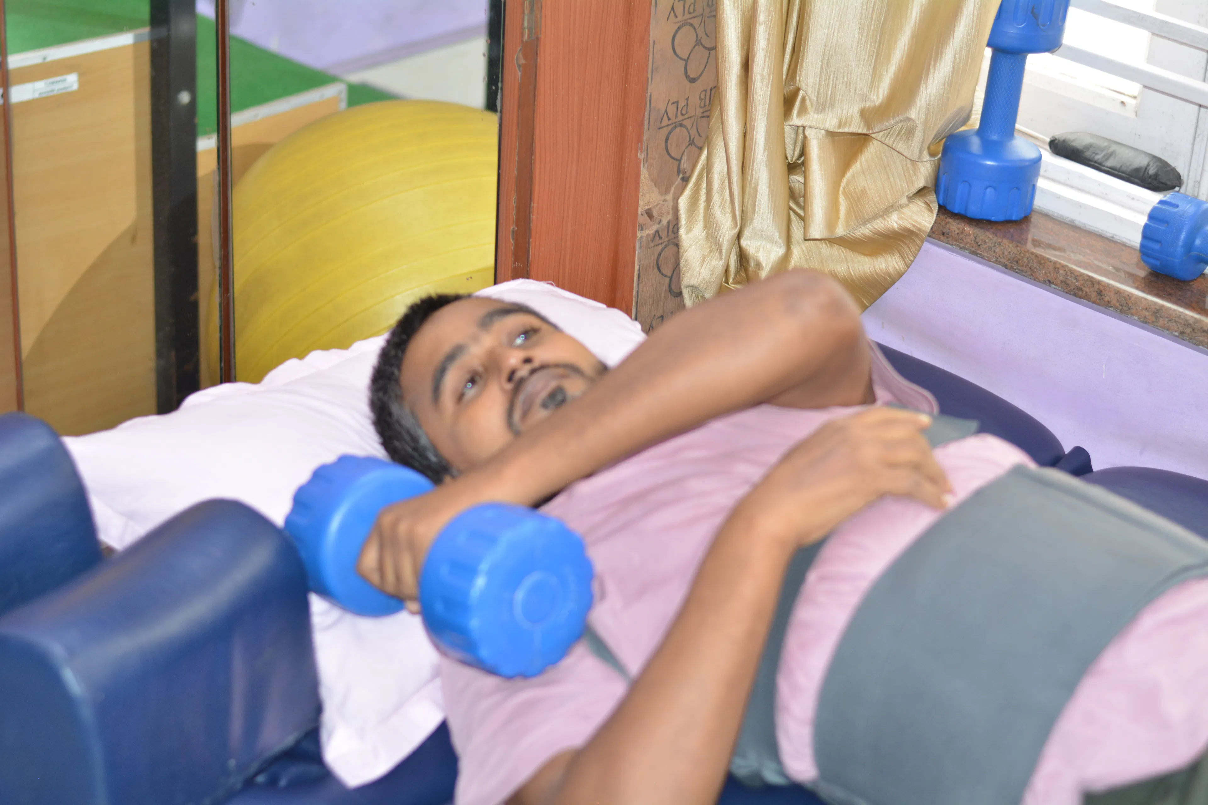 Patient lying on a mat lifting dumbbells during a neuro physio session