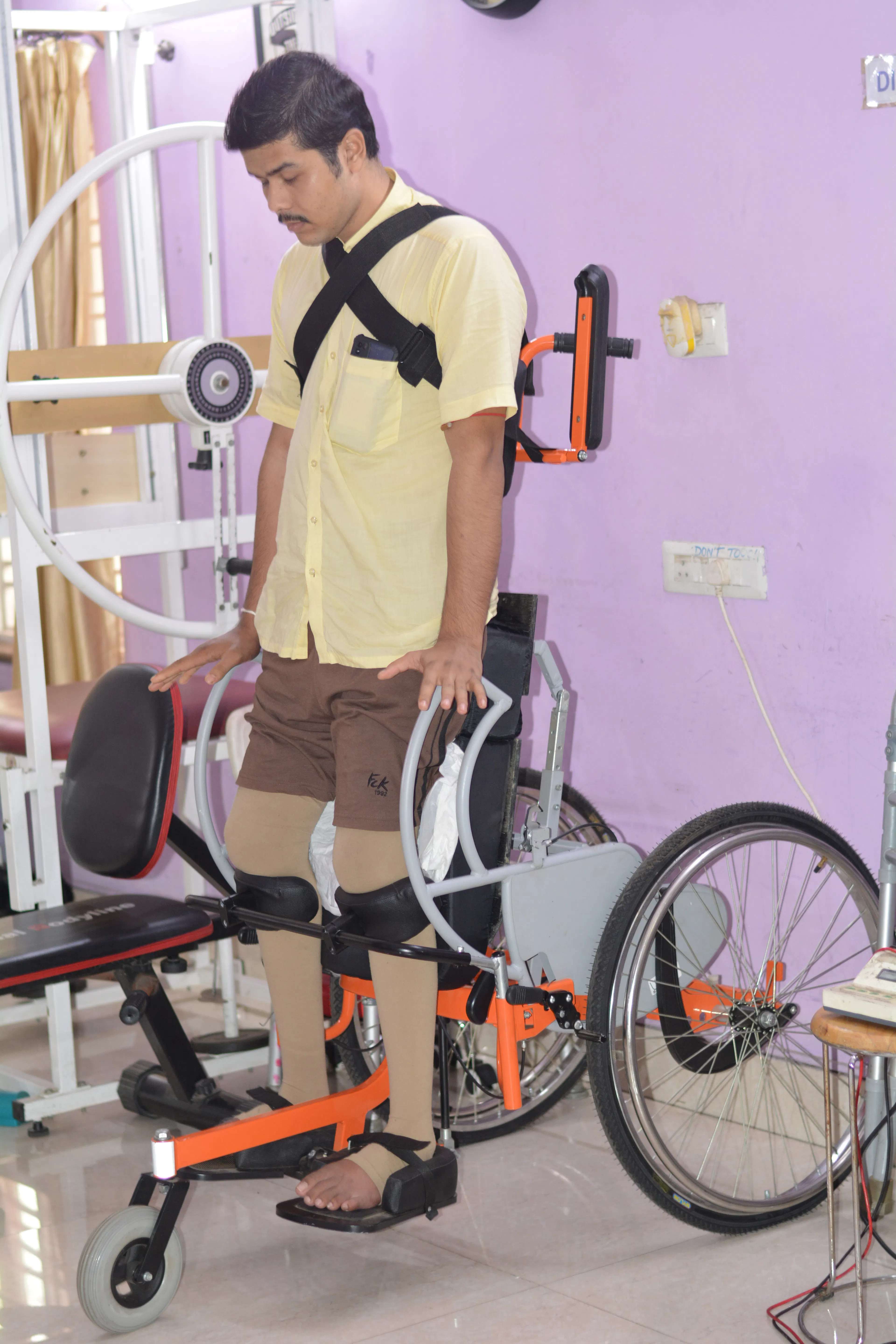 Young man in knee orthoses beside a gait trainer frame during a block of robotic rehabilitation