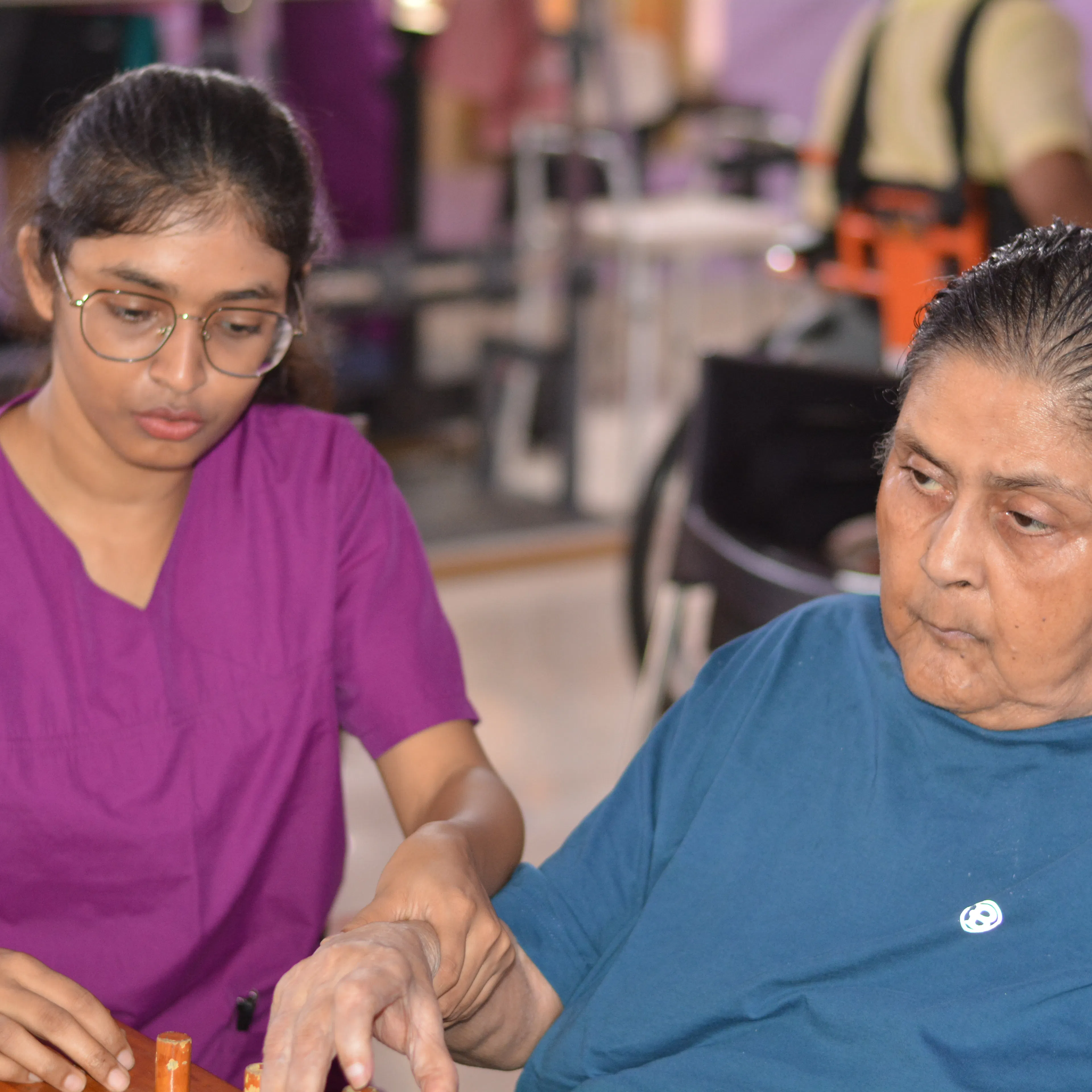 Therapist working closely with an elderly woman on a tabletop task in a therapy session