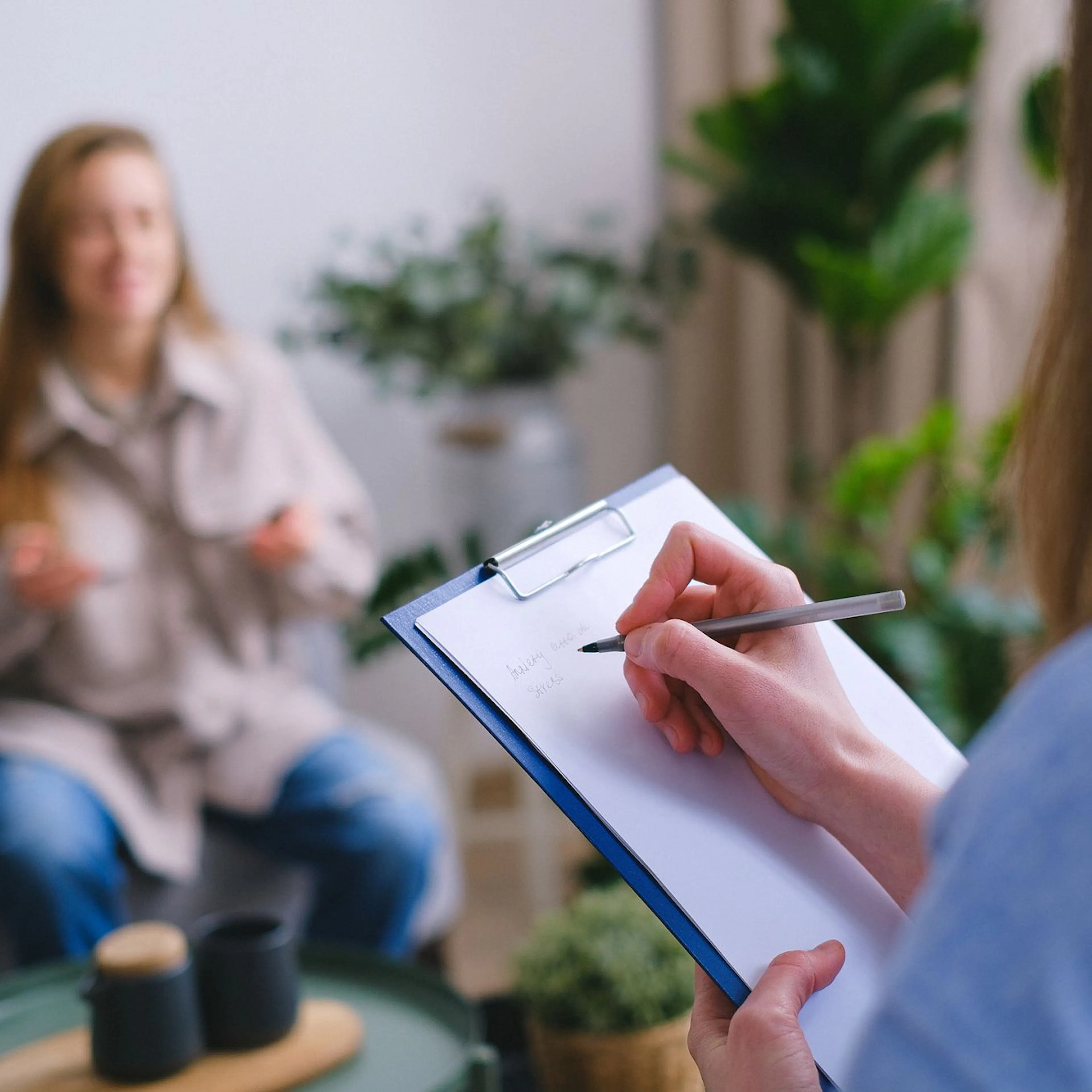 Therapist taking notes while a client speaks, reviewing speech therapy progress
