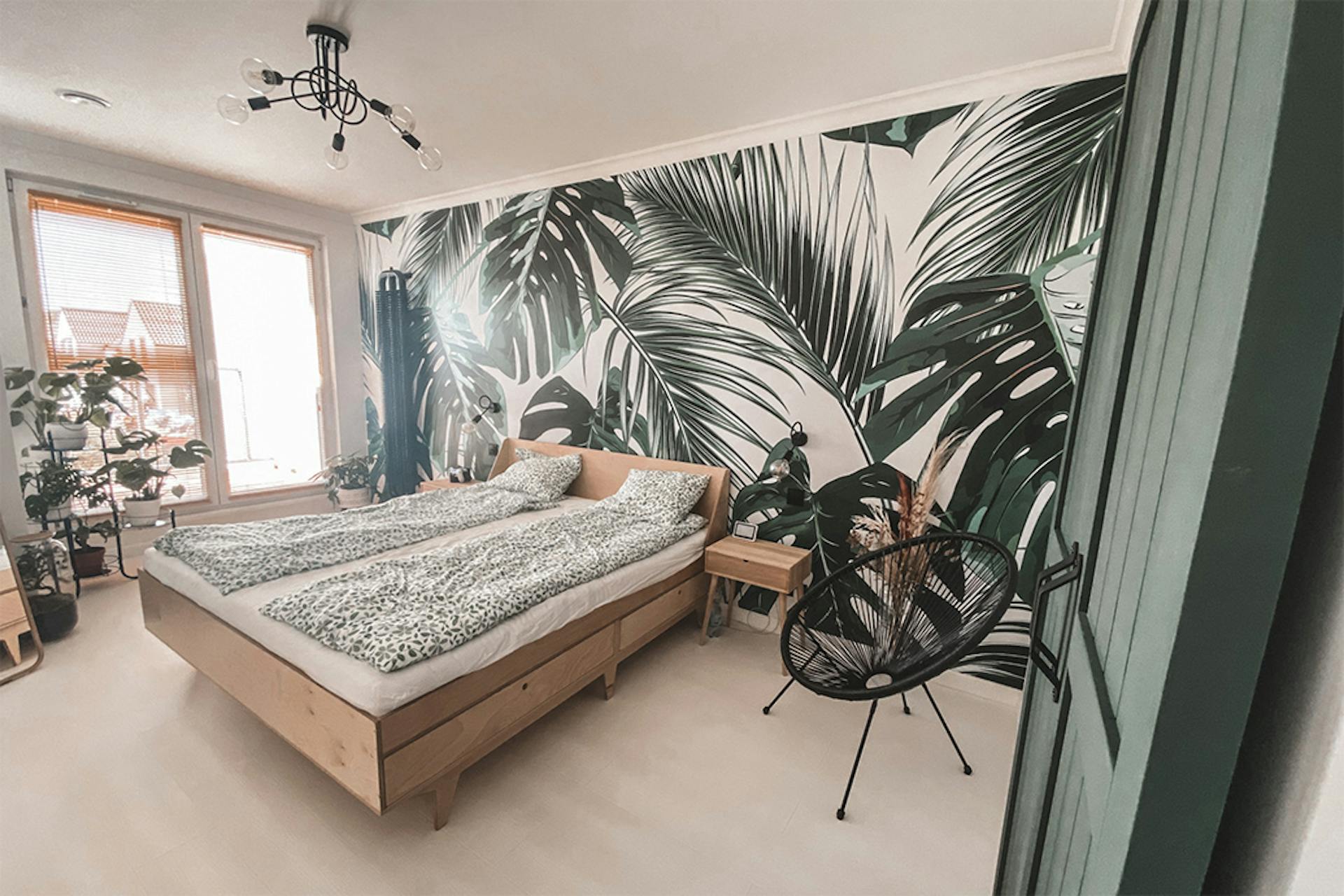 grüne Türen, helles Holz im Schlafzimmer, helles Holz und Grün, Grün im Schlafzimmer, Pflanzenmotiv im Schlafzimmer, botanische Tapete, dekorative Tapete im Schlafzimmer, Leinen mit Blumenmotiv, Pflanze im Schlafzimmer, industrieller Kronleuchter im Schlafzimmer , schwarzer durchbrochener Sessel, helles Holzbett, kleine Nachttisch aus hellem Holz
