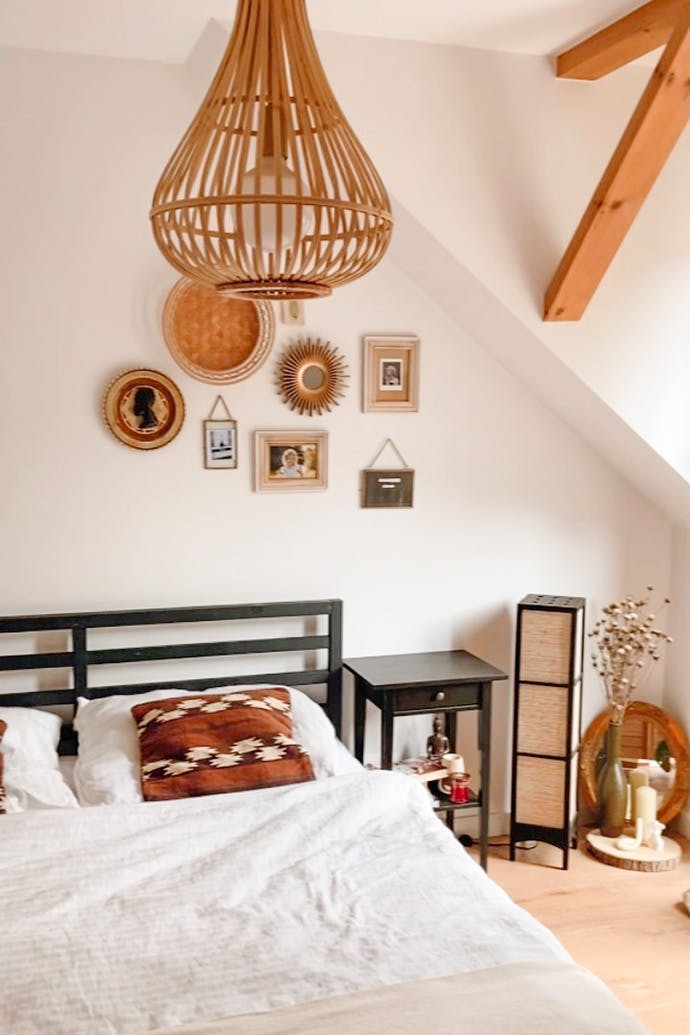 Lampenschirm aus Bambus, schwarzes Rahmenbett, weiße Wände im Schlafzimmer, Dekorationen im Boho-Stil über dem Bett im Schlafzimmer, Holzbalken an der Decke im Schlafzimmer, schwarzer Nachttisch, Boho-Dekorationen im Schlafzimmer im natürlichen Stil