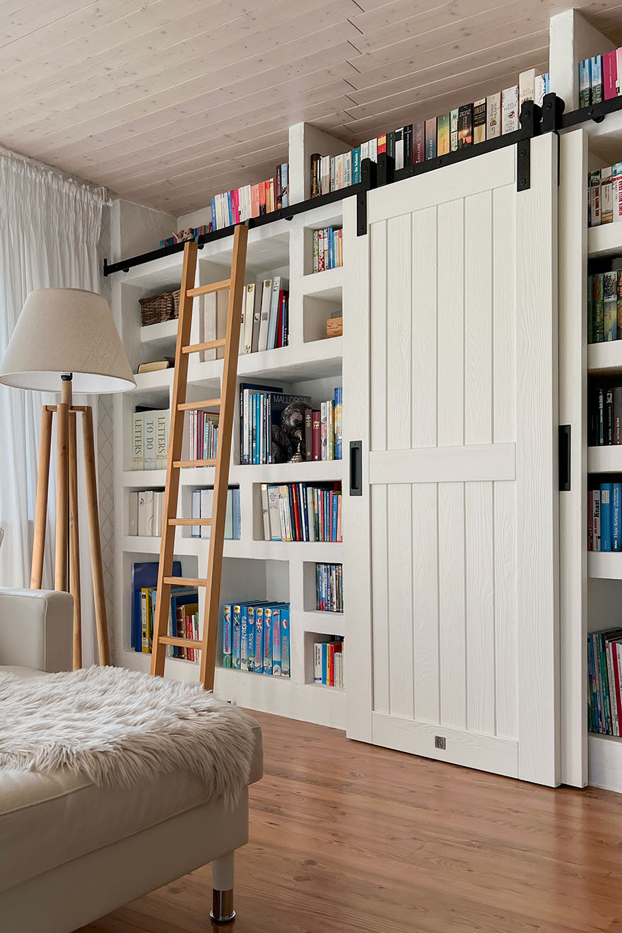 drabinka i białe drzwi przesuwne w aranżacji domowej biblioteki w salonie