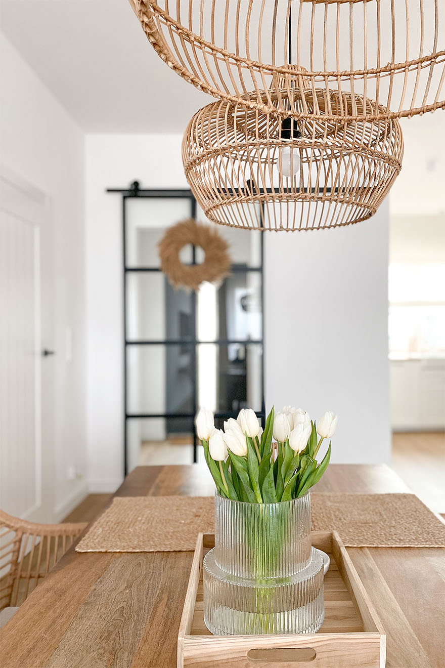 Eine Glasvase auf einem Holztablett und Korblampen schmücken ein Wohnzimmer mit weißen Wänden