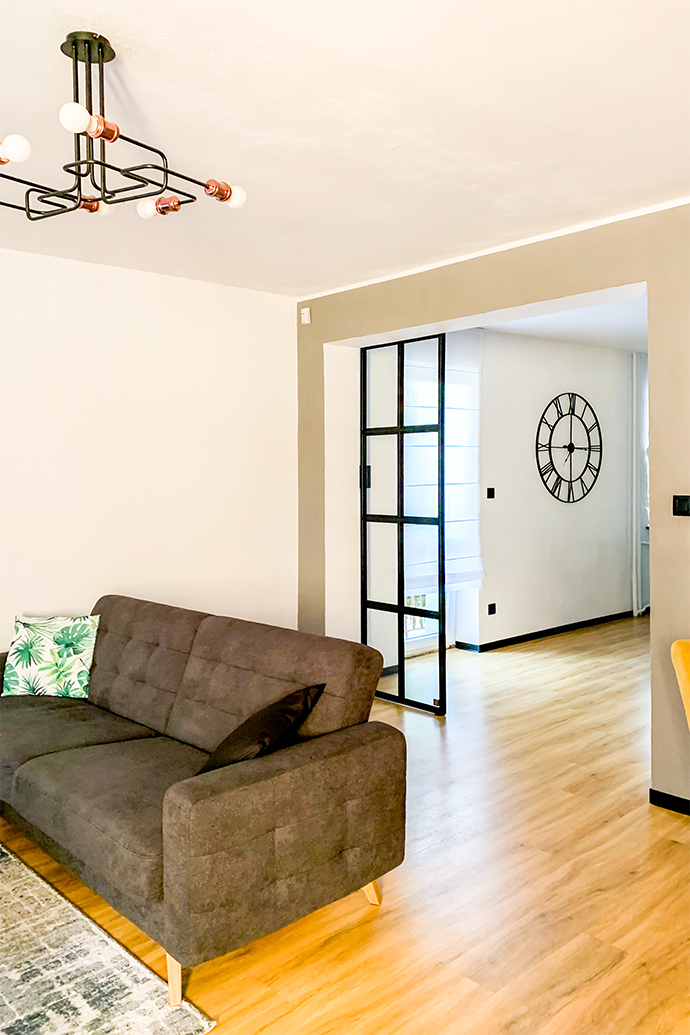 Loft-Innenraum, Glastür in einem Metallrahmen, Glasschiebetür, Industrielampe im Wohnzimmer, graues Sofa, offenes Wohnzimmer, industrielle Wanduhr