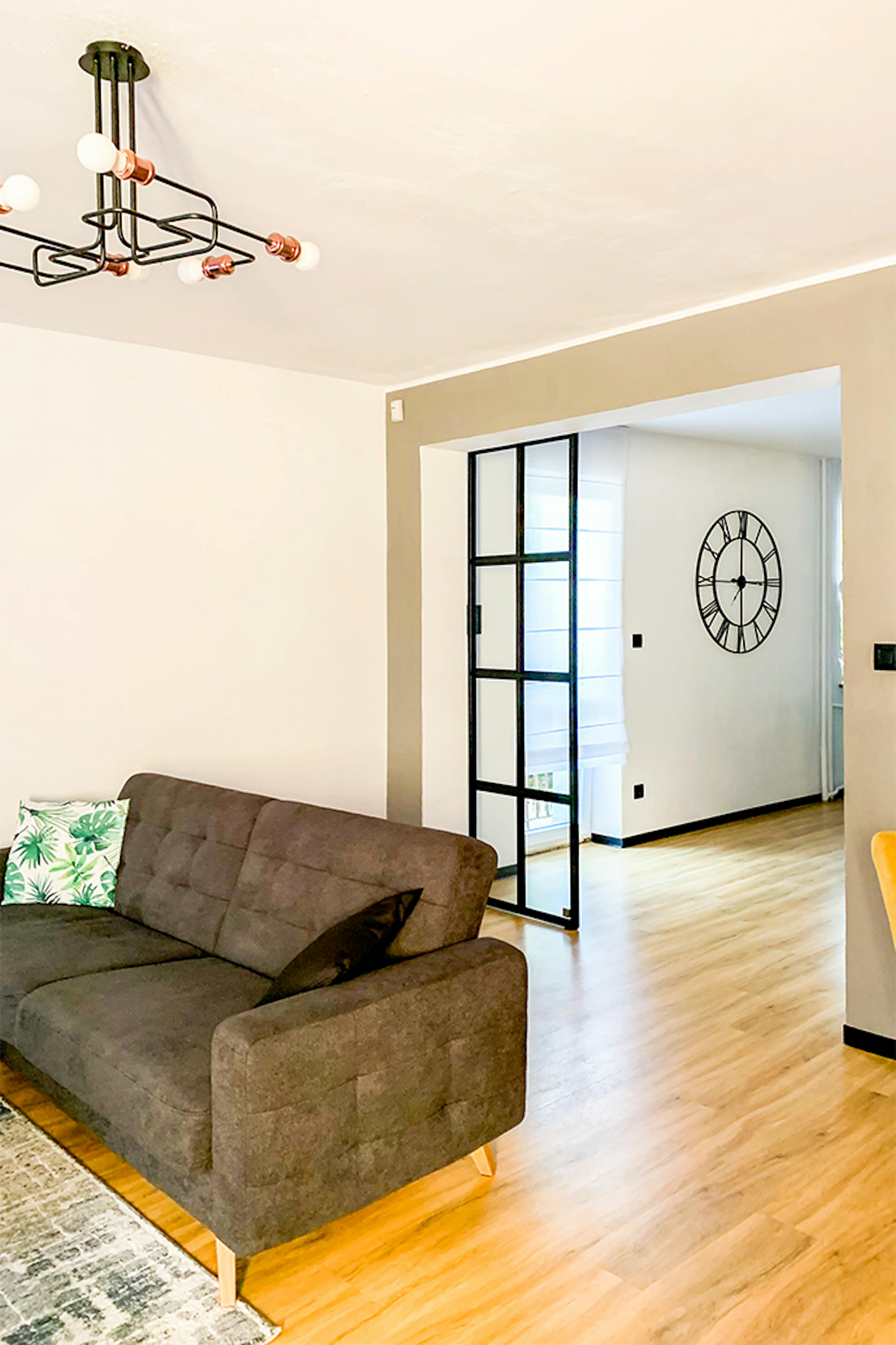 loftowe wnętrze, szklane drzwi w metalowej ramie, szklane drzwi przesuwne, industrialna lampa w salonie, szara sofa, otwarty salon, industrialny zegar na ścianę