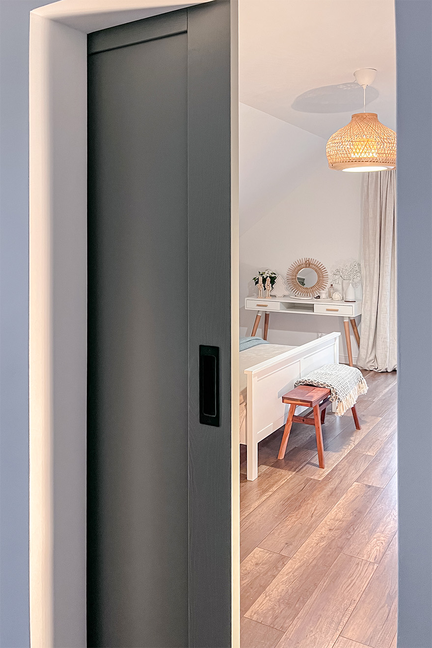 otwarte drzwi ukazujące fragment sypialni z łóżkiem i toaletką