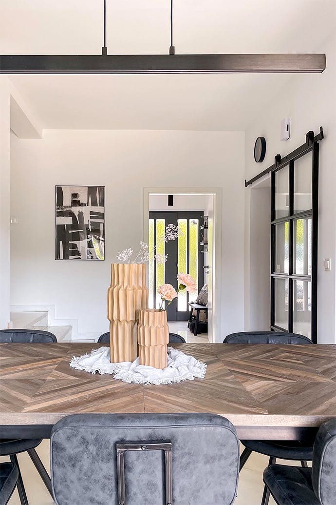 dekoracyjne wazony na dużym stole w jadalni oświetlonym długą minimalistyczną lampą