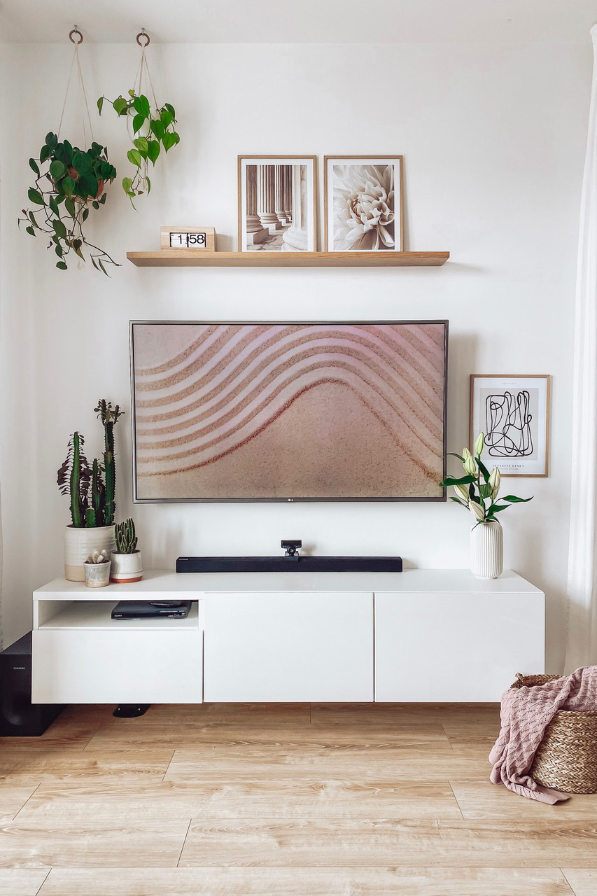 weißer Fernsehschrank, dekorative Bilder in Rahmen an einer weißen Wand, Topfpflanzen im Wohnzimmer