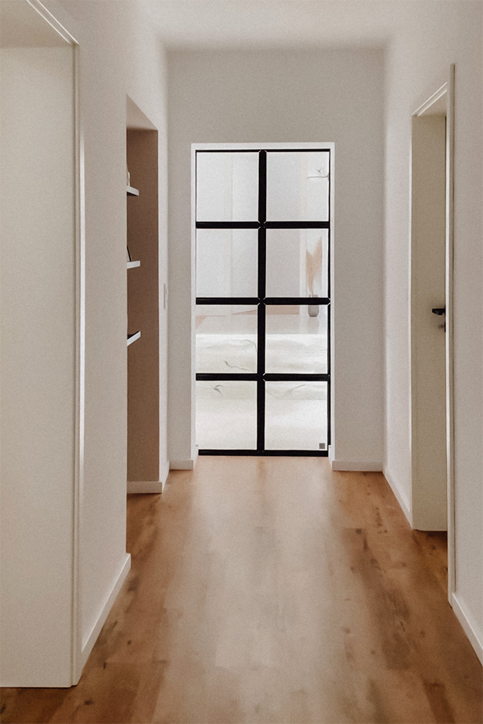 Glastür am Ende des Flurs, der zum Wohnbereich des Hauses führt, Flur mit hellen Wänden, minimalistische Einrichtung des Flurs