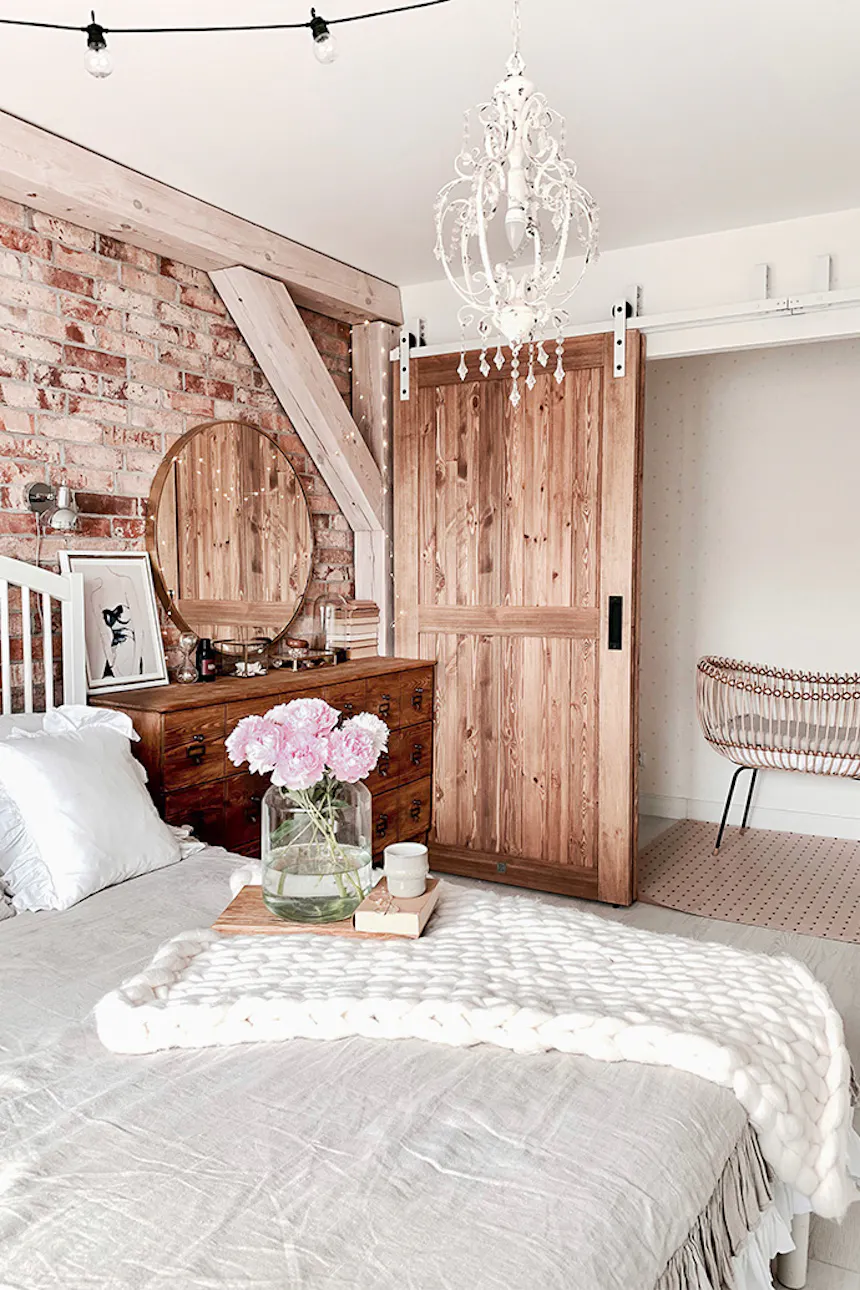 drzwi przesuwne drewniane, drzwi przesuwne naprzemienne, styl rustykalny we wnętrzach, styl modern rustic, drzwi w stylu „barn door”, biały system przesuwny, system przesuwny do drzwi naprzemiennych, cegła na ścianie w sypialnii, belki stropowe w sypialni, biały żyrandol rustykalny