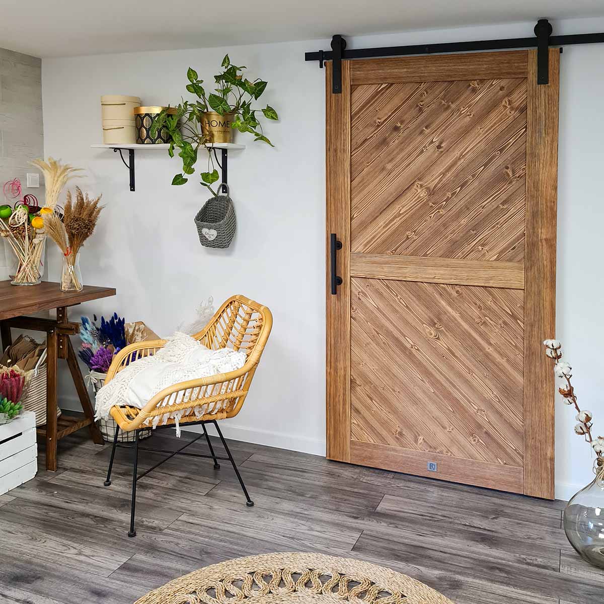 runder geflochtener Juteteppich, Holzschiebetür, schwarzes Schiebesystem, weiße Wände und dunkler Boden in skandinavischem Interieur, Korbstuhl mit Metallbeinen und dekorativem Kissen