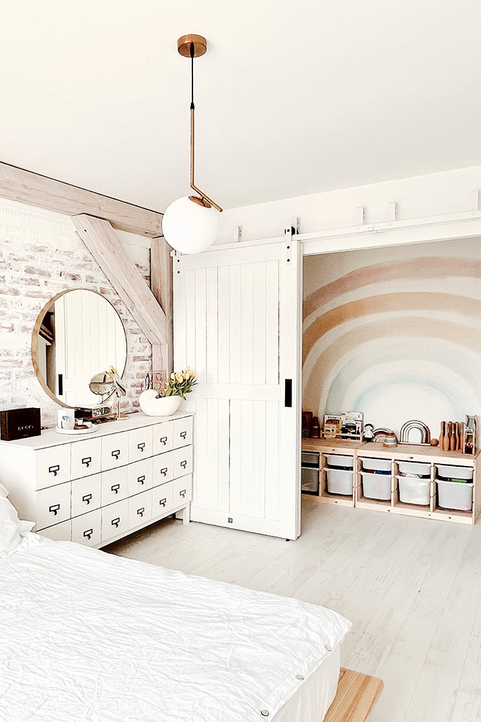weißes schlafzimmer, Aussparung hinter Schiebetüren versteckt, weiße Kommode, weißes Holz im Schlafzimmer, Spielbereich in der Aussparung im Schlafzimmer, Ziegel an der Wand im Schlafzimmer, modernes rustikales Schlafzimmer