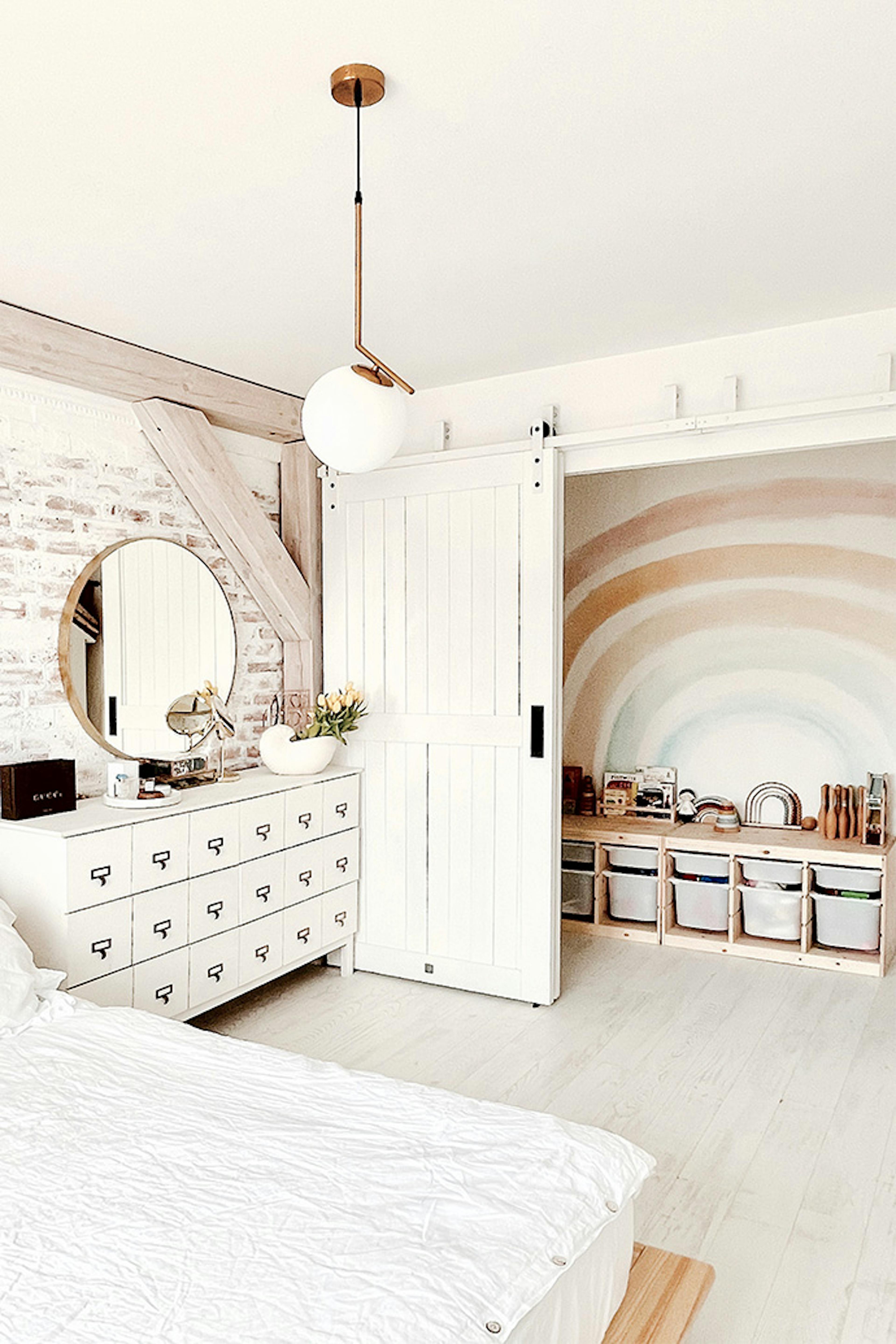weißes schlafzimmer, Aussparung hinter Schiebetüren versteckt, weiße Kommode, weißes Holz im Schlafzimmer, Spielbereich in der Aussparung im Schlafzimmer, Ziegel an der Wand im Schlafzimmer, modernes rustikales Schlafzimmer