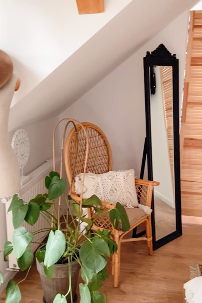 großer Standspiegel in schwarzem Rahmen, Korbstuhl, dekoratives Kissen mit Fransen, große Blume in einem Topf in einem natürlichen Schlafzimmer