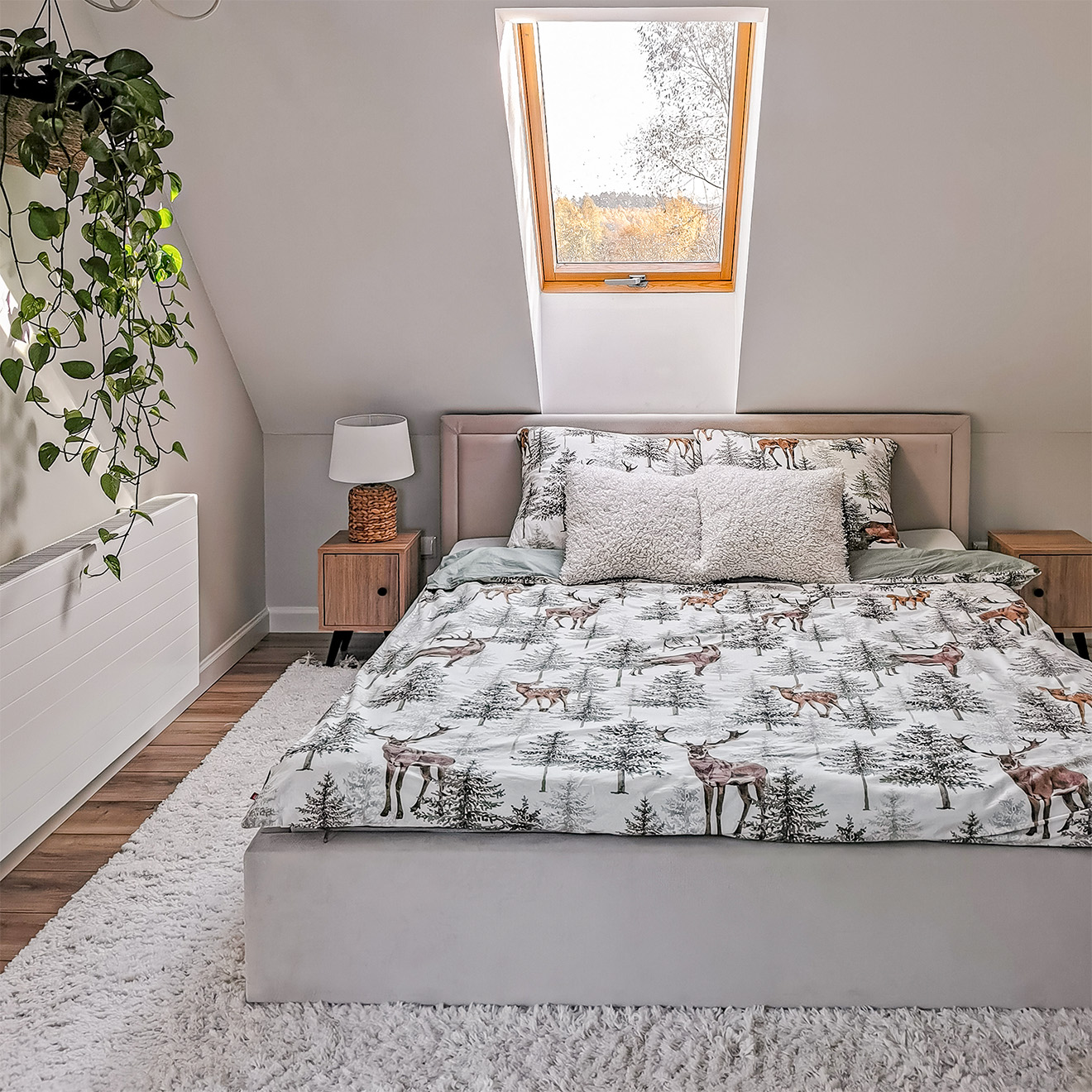 Bettwäsche mit Waldmotiven auf einem Polsterbett mit Kopfteil unter dem Dachfenster