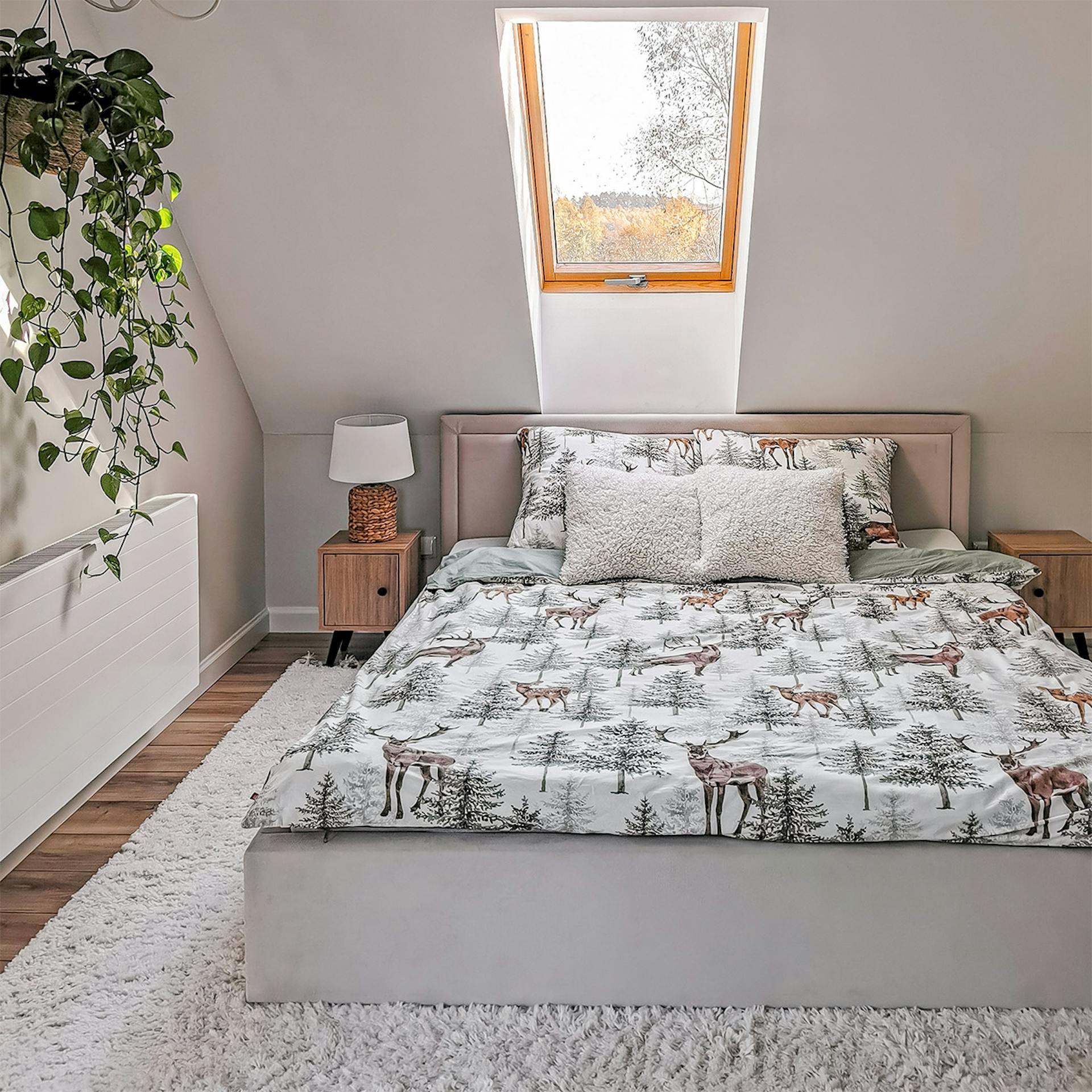 Bettwäsche mit Waldmotiven auf einem Polsterbett mit Kopfteil unter dem Dachfenster