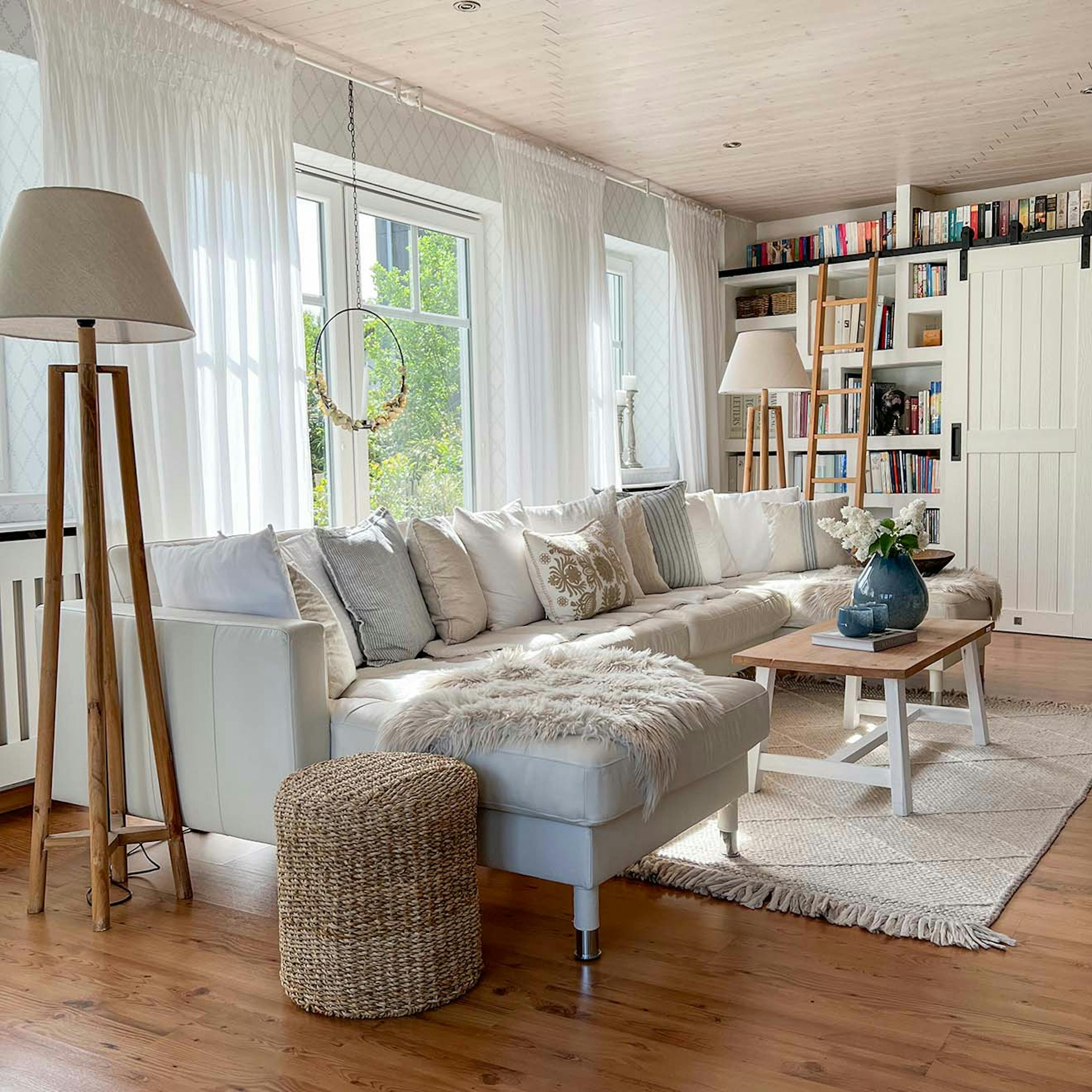 jasnoszara sofa, drewniana podłoga w salonie z biblioteką