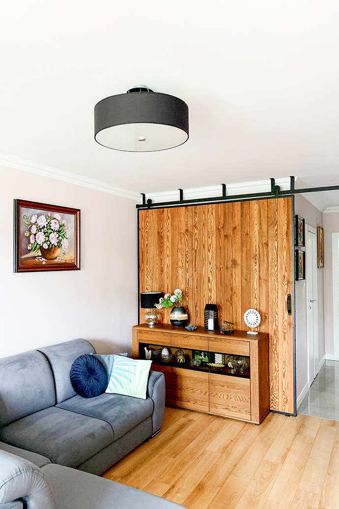 große Schiebetür in einem Metallrahmen, Bilder an der Wand, graues Sofa, Holzschiebetür, Kommode aus Holz