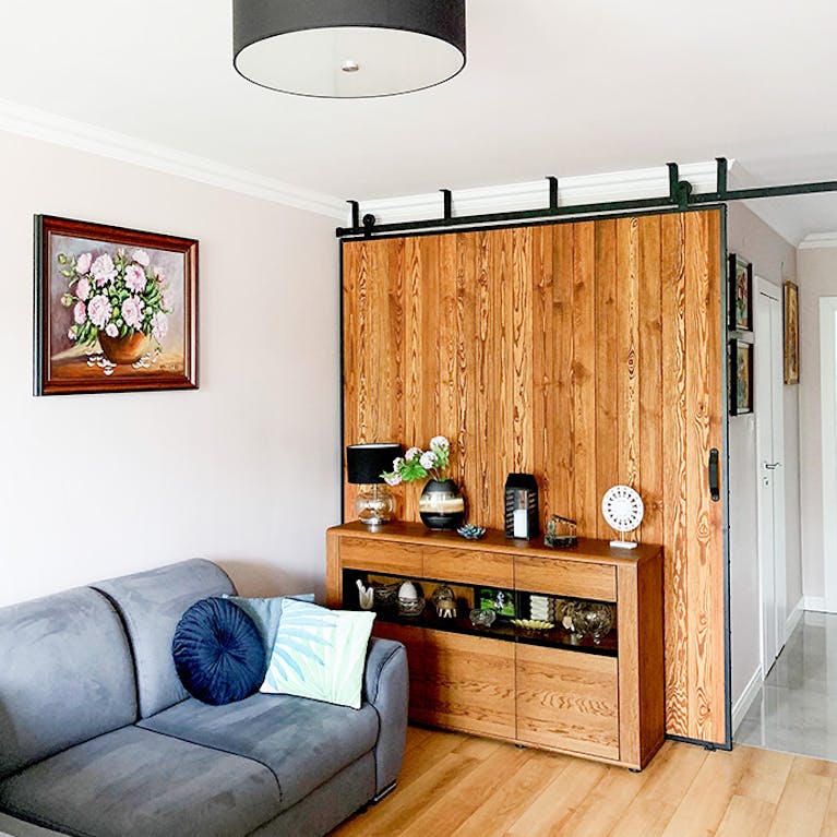 large sliding door in a metal frame, pictures on the wall, grey sofa, wooden sliding door, wooden chest of drawers