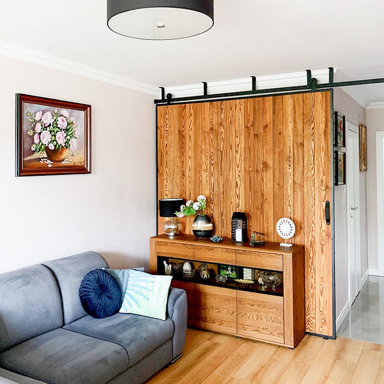 large sliding door in a metal frame, pictures on the wall, grey sofa, wooden sliding door, wooden chest of drawers
