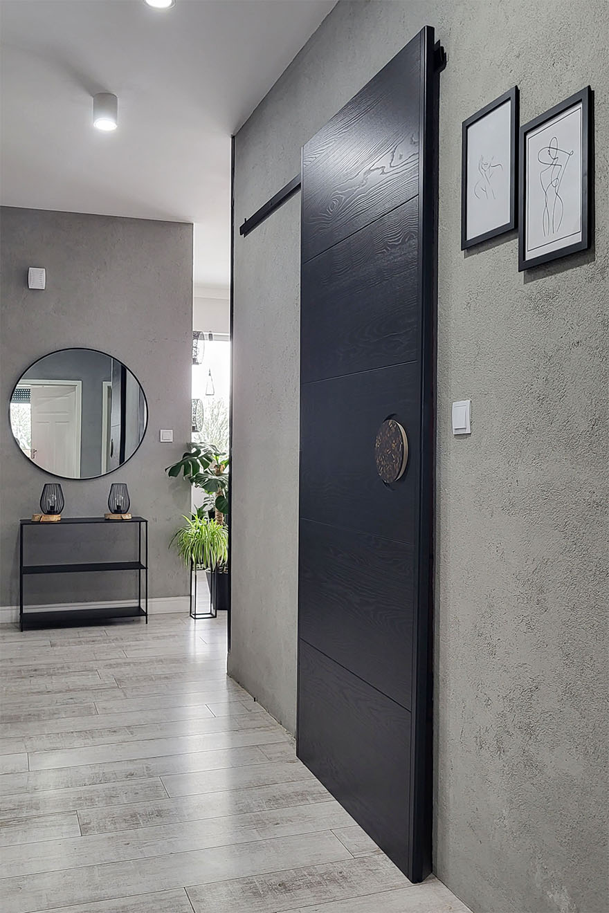 czarne drzwi przesuwne w wejściu do łazienki w korytarzu z szarymi ścianami