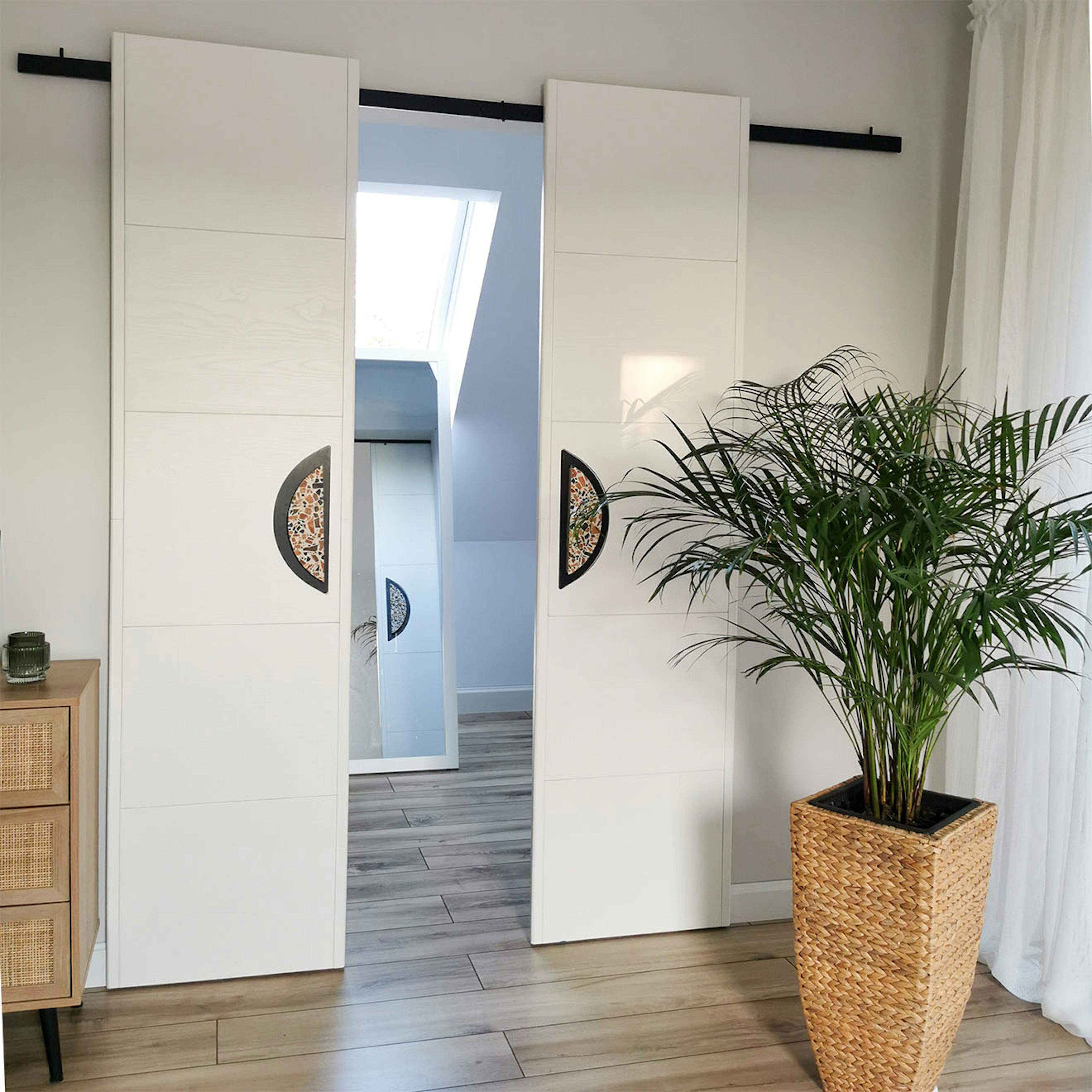 minimalistische, doppelte Schiebetüren mit großen Griffen, die einen kleinen Kleiderschrank schließen