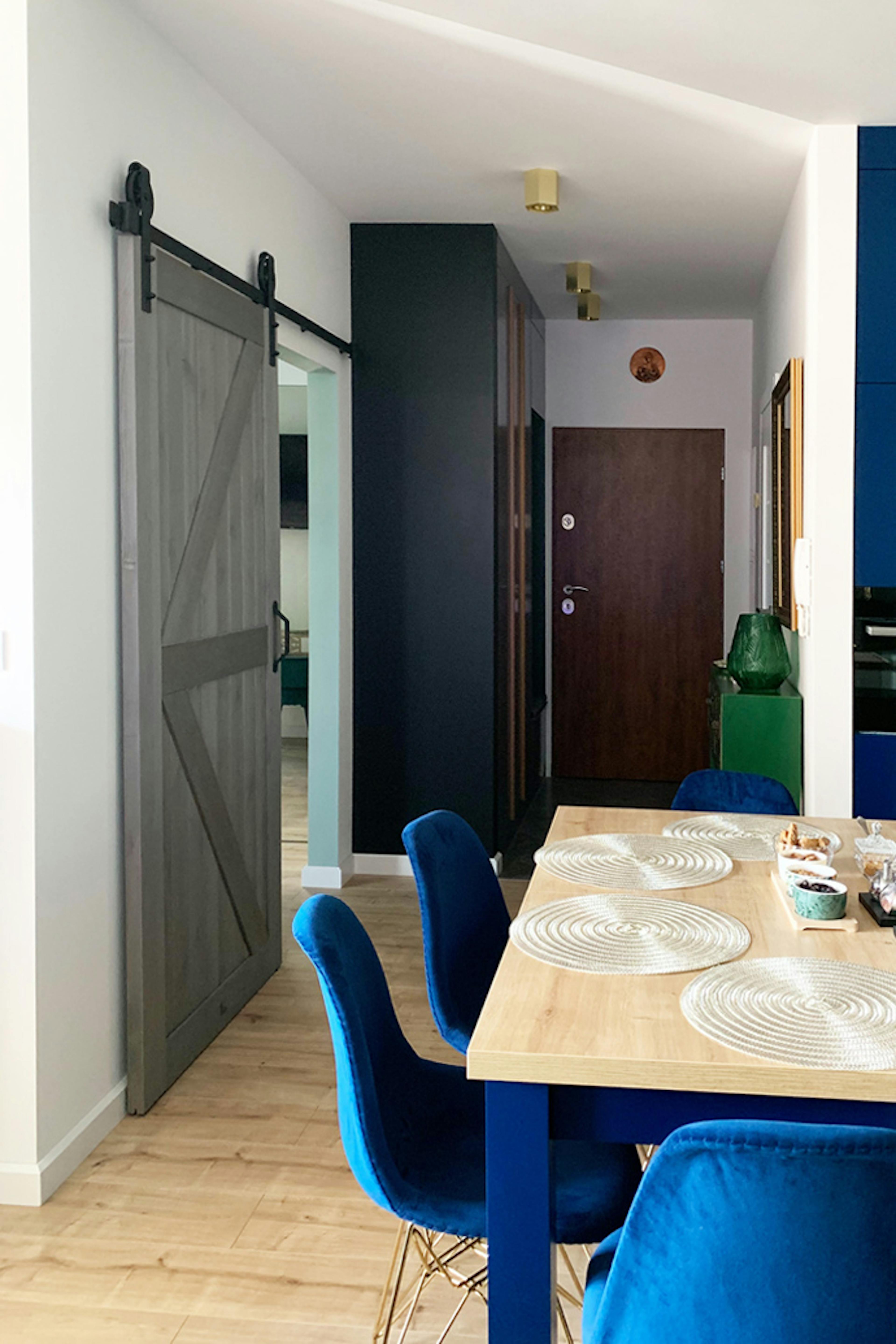 Holzschiebetür, Scheunen-Schiebetüren Schiebetür holz grau, goldene Accessoires im Innenraum, modernes Interieur, offener Raum, Küche mit Esszimmer und Wohnzimmer, blaue Stühle für das Esszimmer, Schiebetüren für das Schlafzimmer, klare Farben im Innenraum