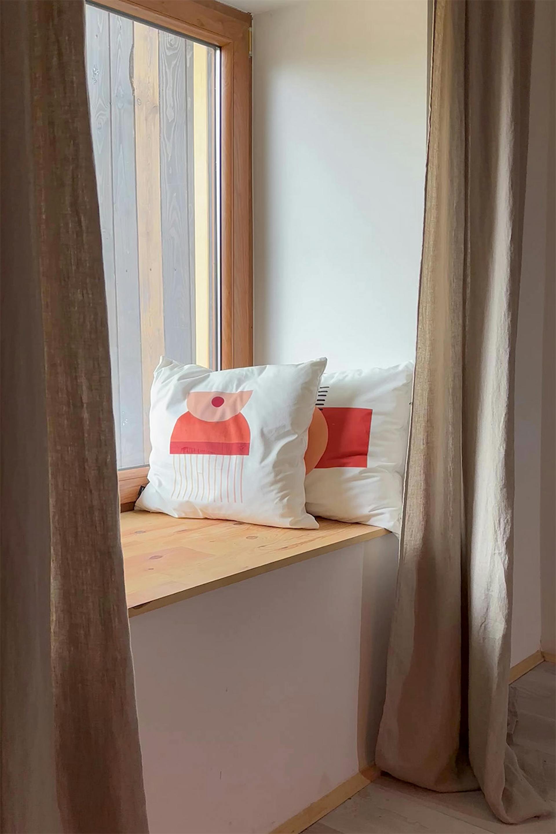 lniane zasłony i dekoracyjne poduszki w aranżacji siedziska przy oknie