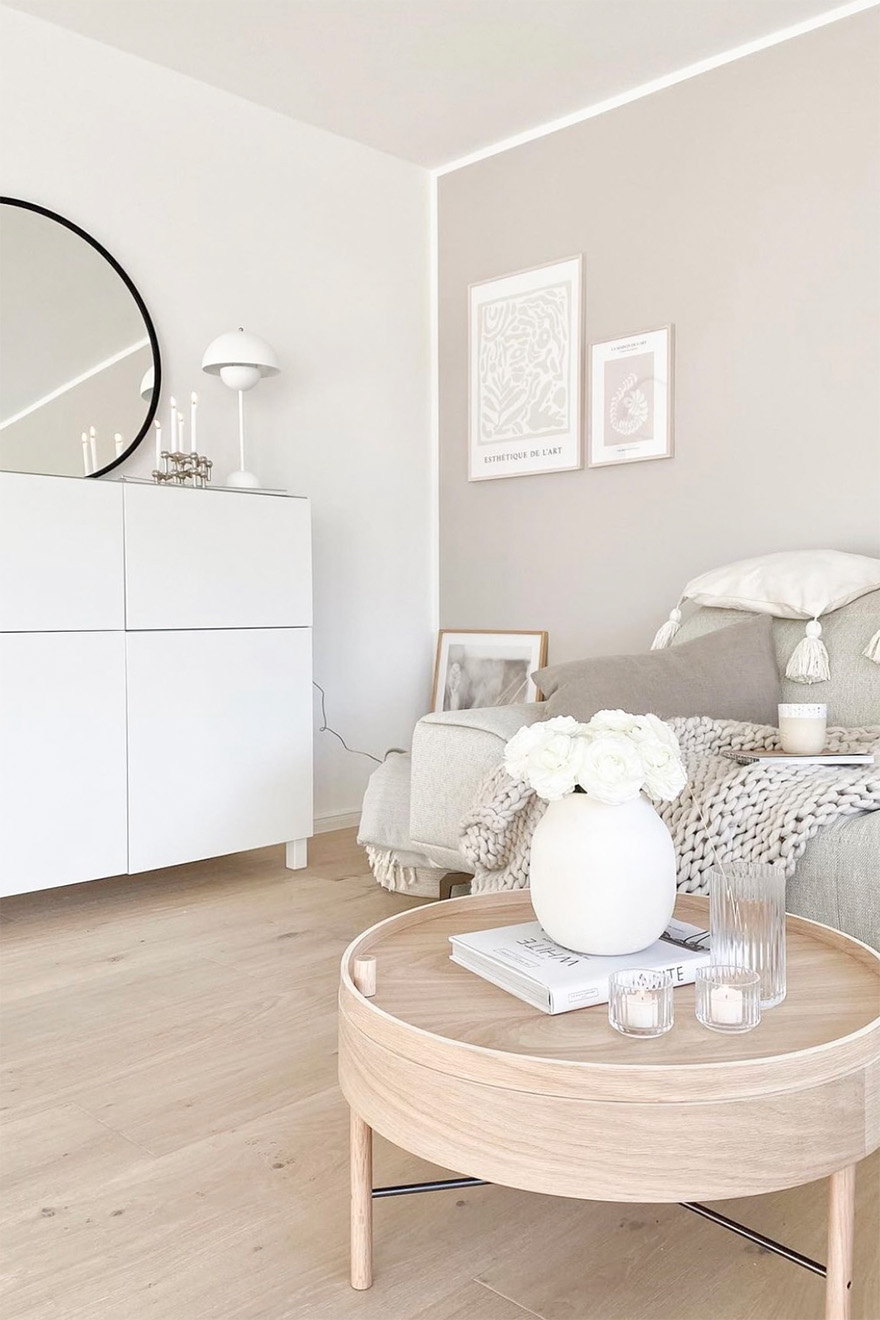 okrągły jasny drewniany stolik kawowy przy beżowej sofie w skandynawskim salonie