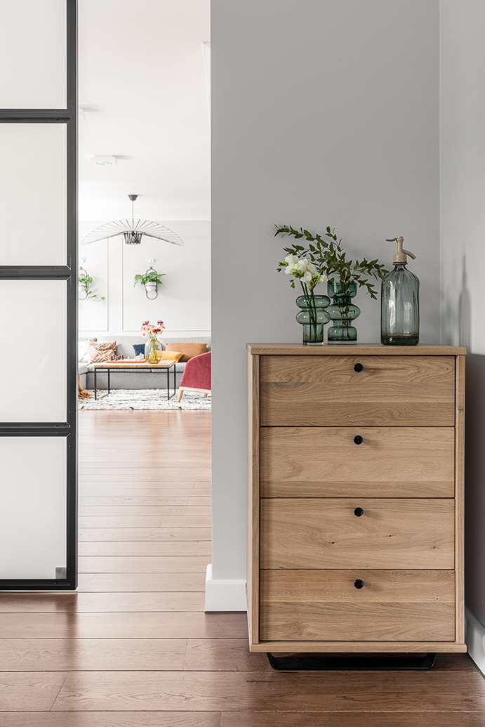 leichte hölzerne Kommode, kleine Kommode im Wohnzimmer, Glas- und Metalltüren, dekorative Glasvasen, Dekorationen auf der Kommode, Glasdekorationen für das Wohnzimmer, heller Raum, Eingang zum großen Wohnzimmer