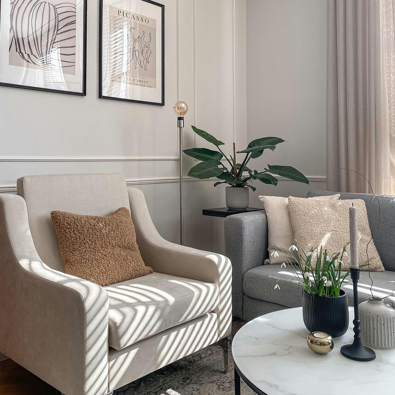 graues Sofa, cremefarbener Sessel, Wohnzimmer im eklektischen Stil, Stuck an der Wand im Wohnzimmer, Poster in einem schwarzen Rahmen an der Wand im Wohnzimmer