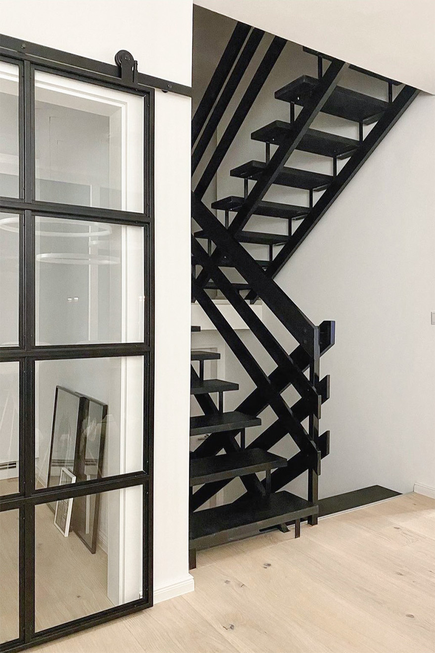 czarne ażurowe schody obok industrialnych drzwi przesuwnych prowadzących do kuchni