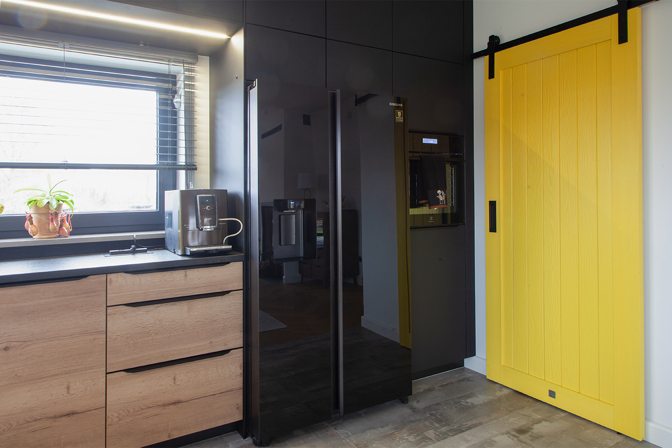 żółte drzwi przesuwne do spiżarni w kuchni z czarnymi szafkami