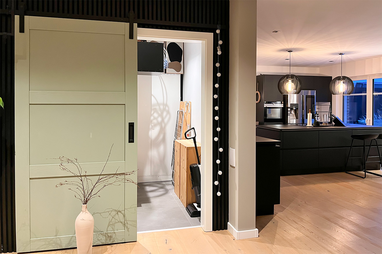 szałwiowo-zielone drzwi przesuwne do spiżarni przy nowoczesnej kuchni z czarnymi meblami