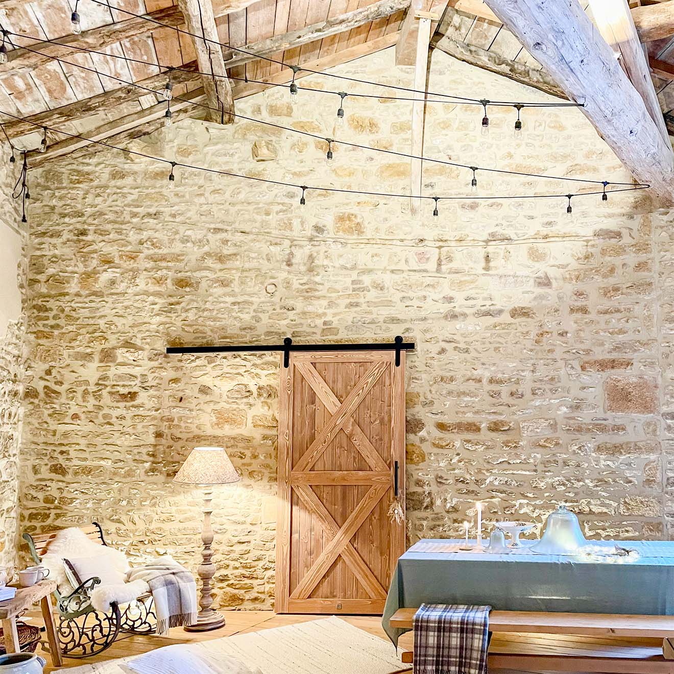 Holztisch, Bänke, Schaukelstuhl und Schiebetüren auf einer überdachten Terrasse, umgeben von Natursteinmauern