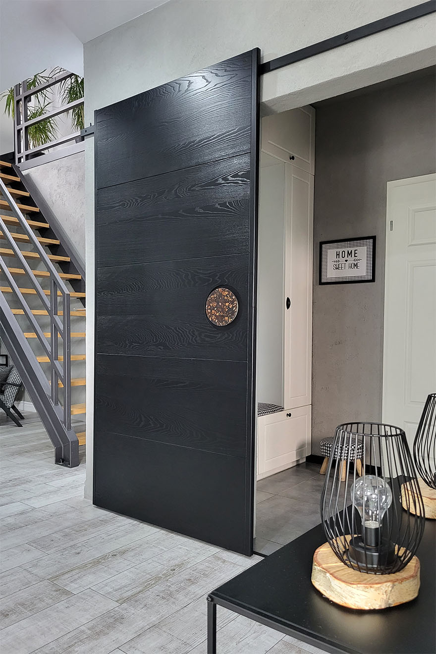 minimalistyczne czarne drzwi przesuwne z designerską klamką w przedpokoju nowoczesnego domu