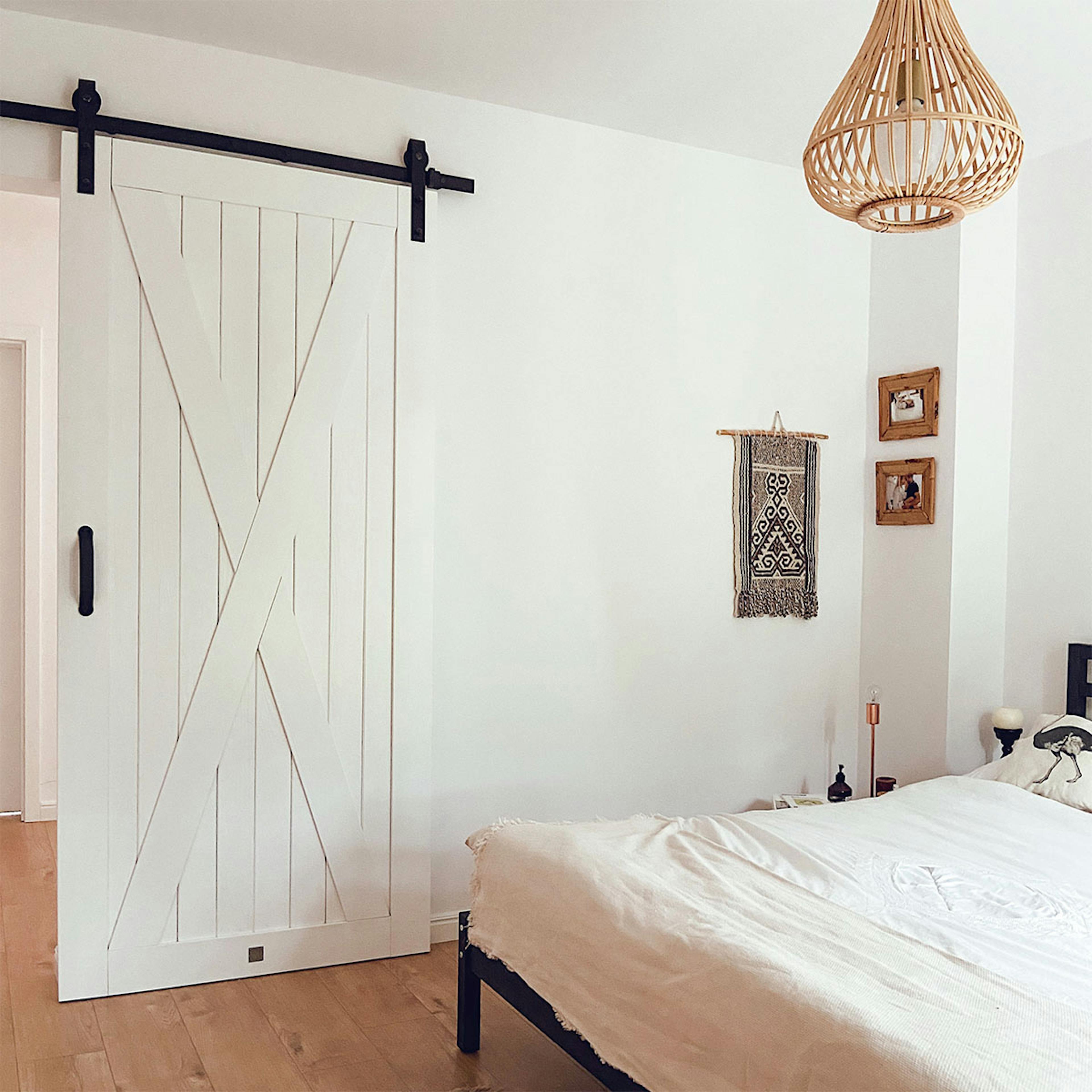 Weiße Massivholz-Schiebetür im Eingang zum natürlichen Schlafzimmer, weiße Wände im Schlafzimmer, Bambus-Pendelleuchte, natürliche Boho-Dekorationen an der weißen Wand