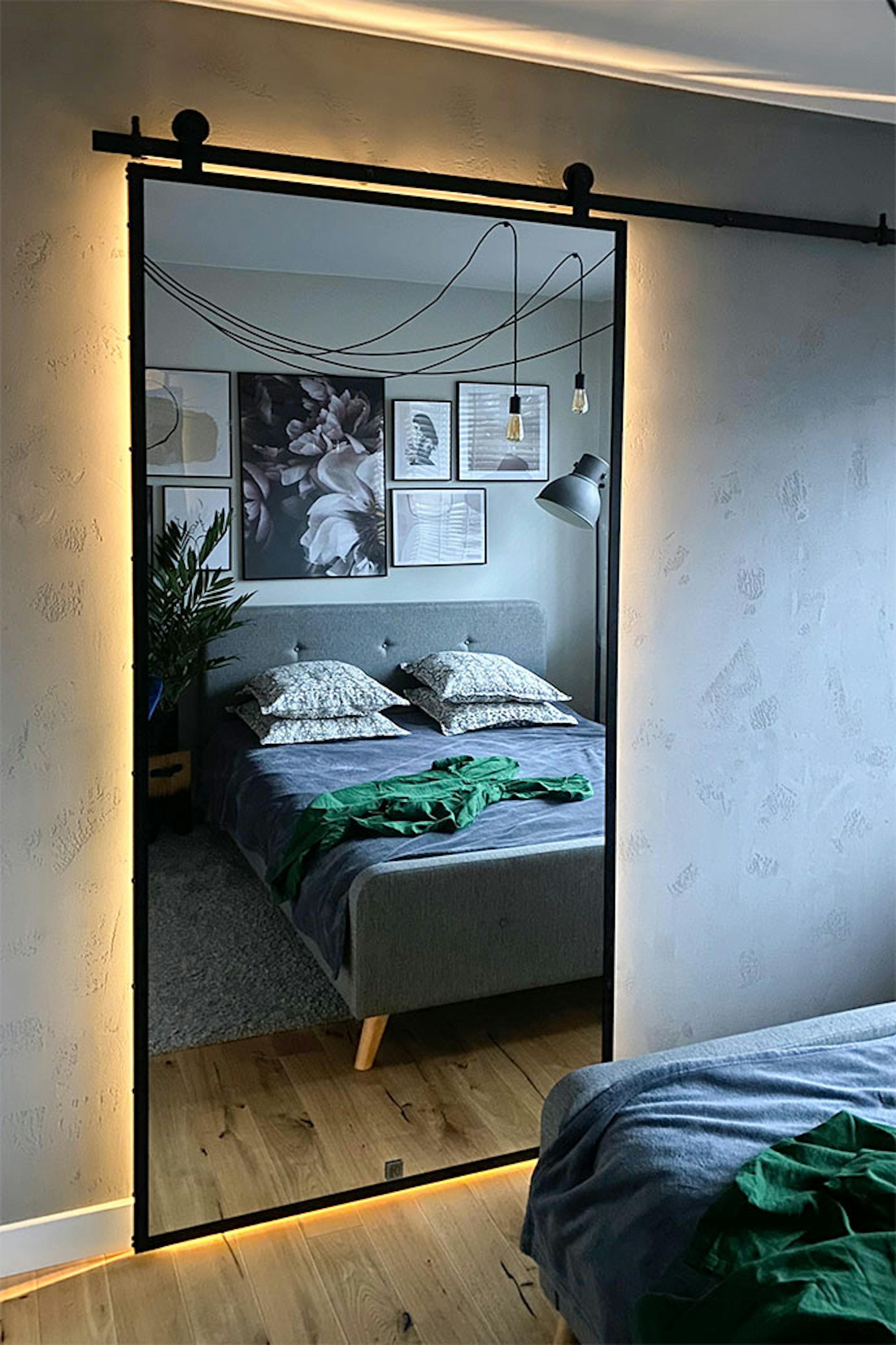 Schiebetüren mit einem großen Spiegel in einem Metallrahmen, die ein Ankleidezimmer in einer Schlafzimmernische im Loftstil schließen