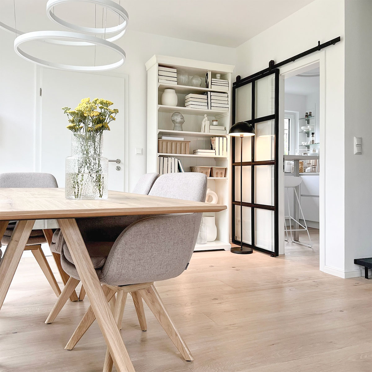 drewniany stół i nowoczesne lampy w jadalni połaczonej z kuchnią drzwiami przesuwnymi ze szkłem