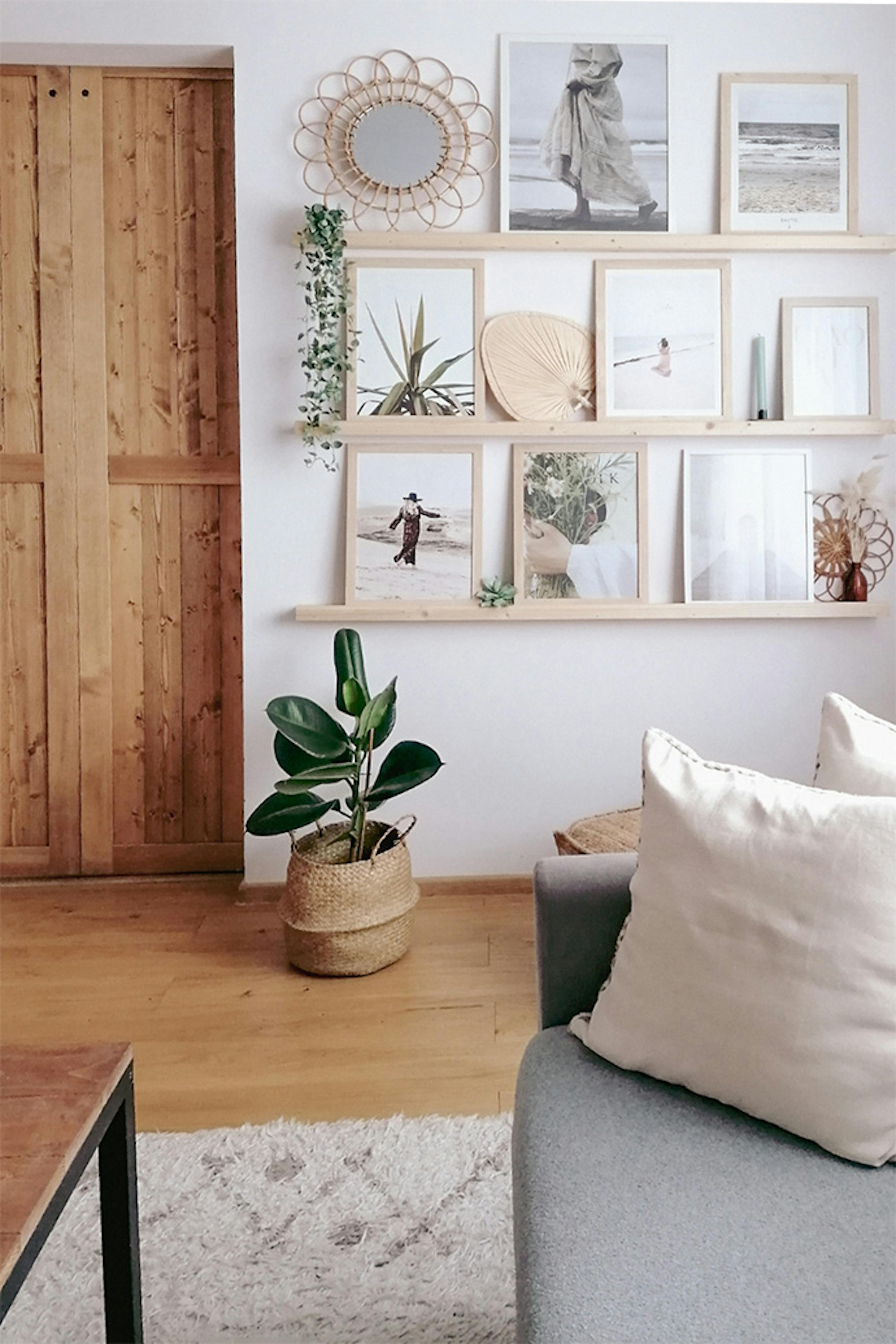 Fotogalerie an der Wand im Wohnzimmer, Fotos in hellen Holzrahmen an der Wand, Holzdekorationen im Wohnzimmer, Wohnzimmer im Boho-Stil, Fotos in Rahmen an der weißen Wand im Wohnzimmer, große Topfblume auf dem Boden im Wohnzimmer