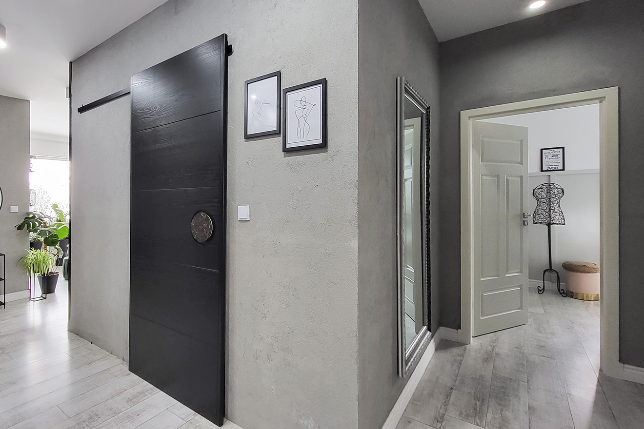 przedpokój z szaro-betonowymi ścianami i czarnymi drzwiami przesuwnymi
