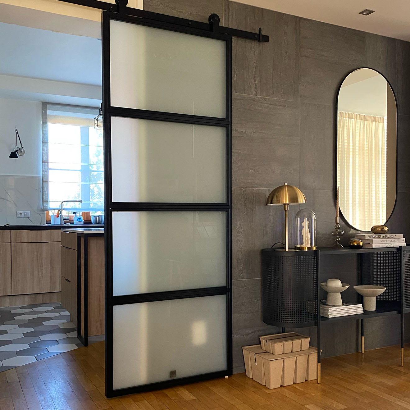 Loft Türen mit glas, Metalltür mit glas für die Küche, helle Küche mit Insel, grafitfliesen an der wand, goldene Lampe auf einer schwarzen Konsole, schwarze durchbrochene Konsole mit spiegel in der flur