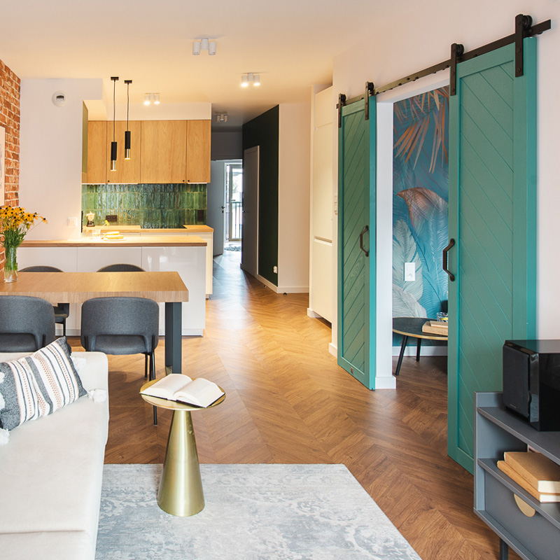 ein Wohnzimmer mit Küchenzeile, das durch eine türkisfarbene Schiebetür vom Schlafzimmer getrennt ist